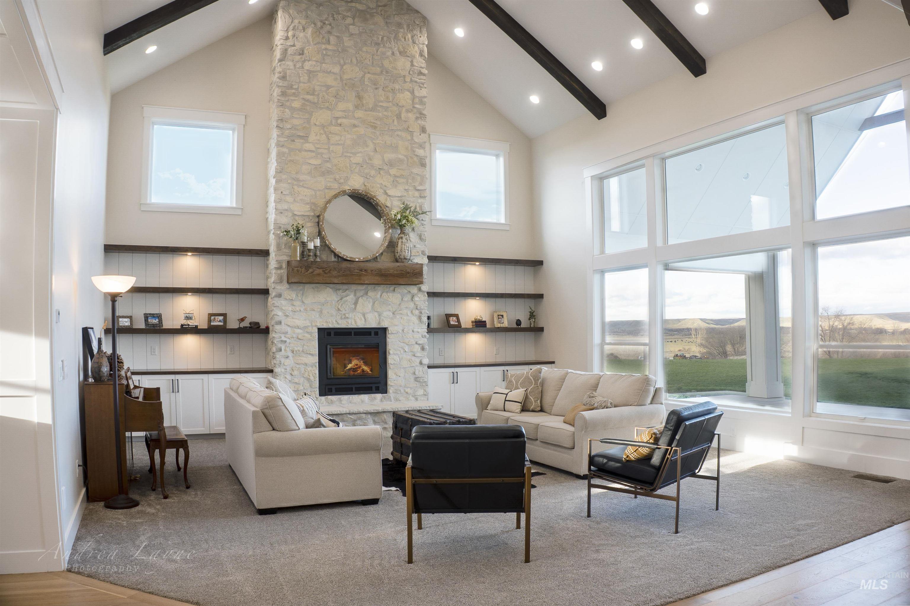 Living area featuring high vaulted ceiling, a stone fireplace, light wood-style flooring, and beam ceiling