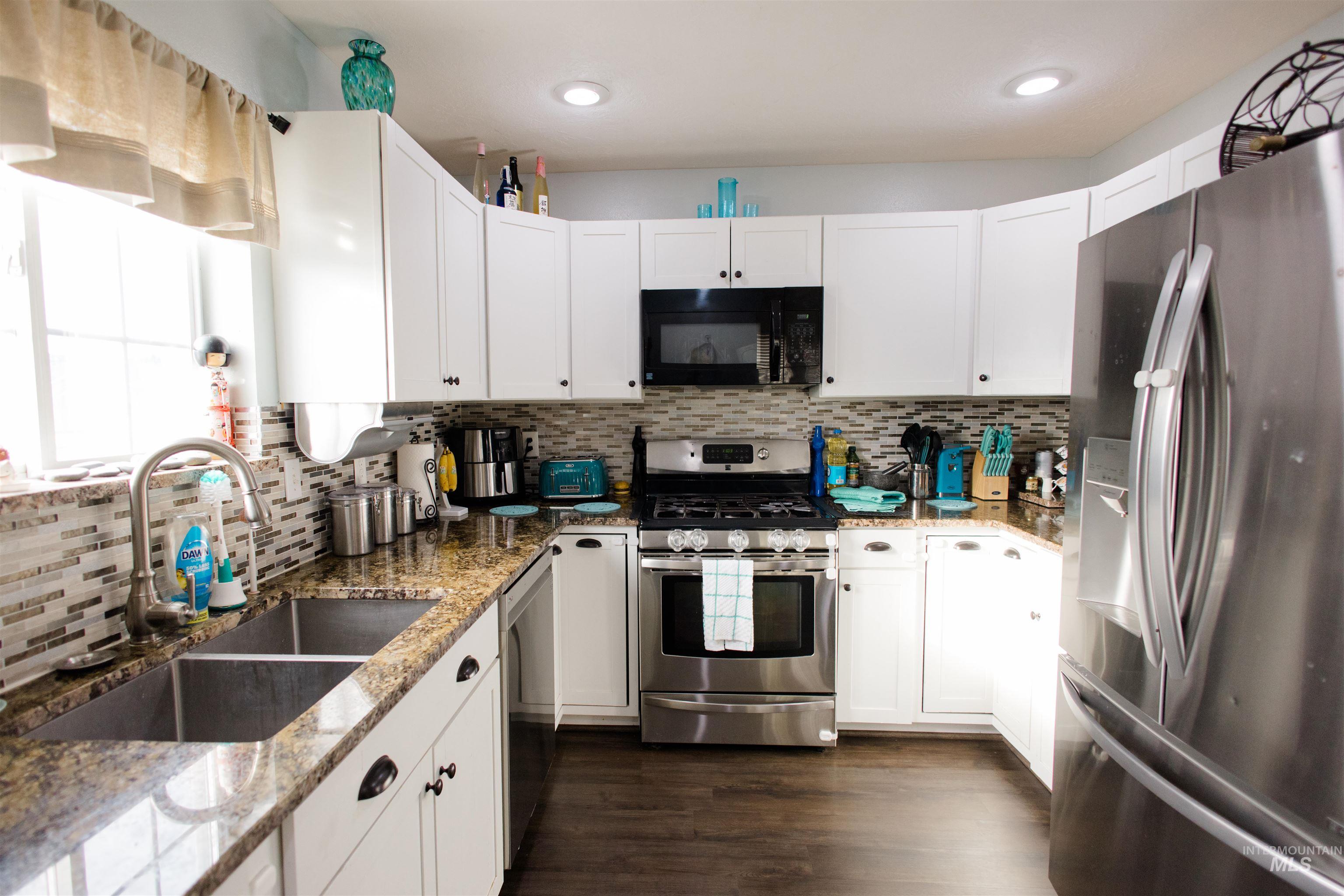 Kitchen featuring appliances with stainless steel finishes, light stone countertops, white cabinets, dark wood finished floors, and recessed lighting
