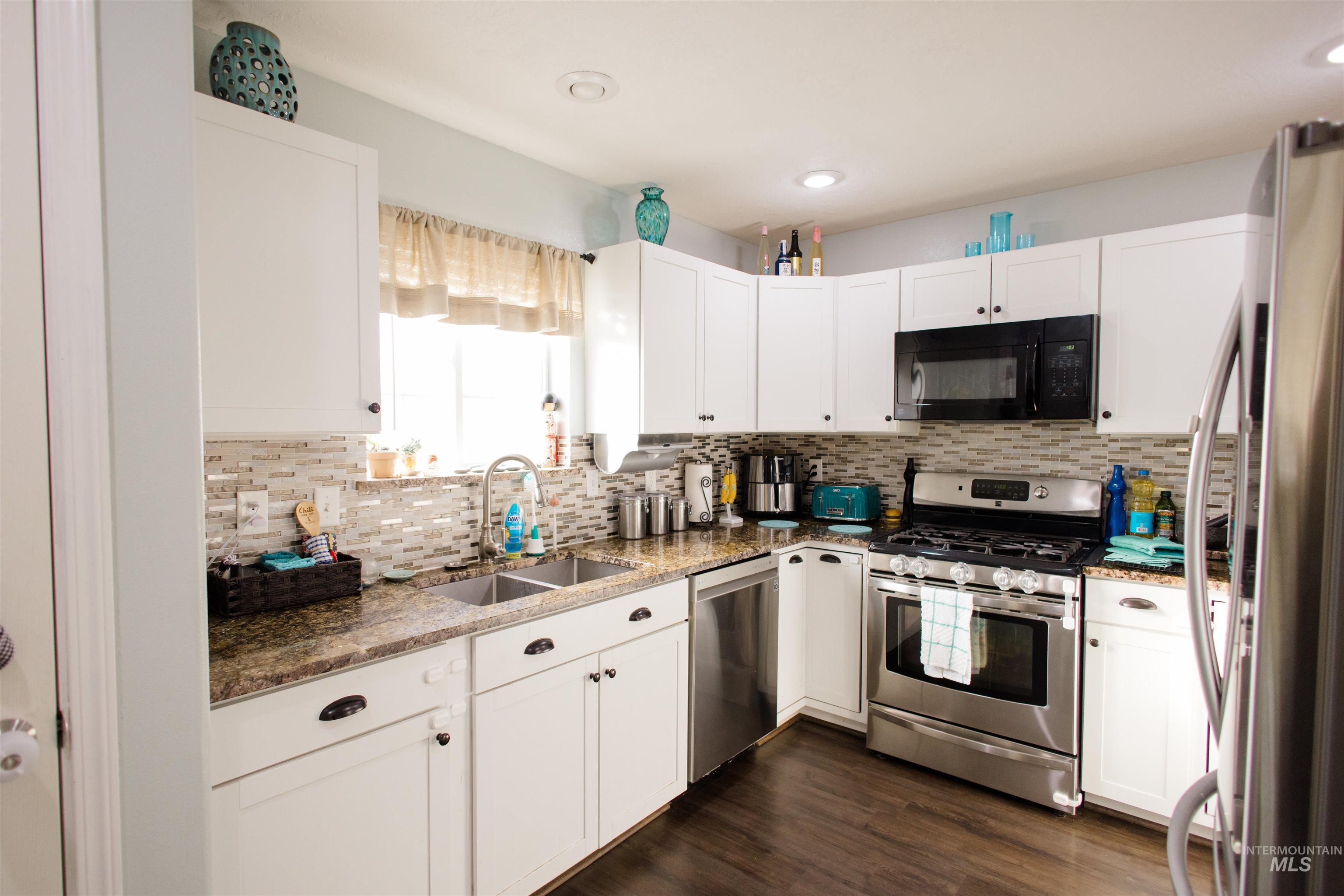 Kitchen with dark stone countertops, white cabinetry, appliances with stainless steel finishes, dark wood-style flooring, and backsplash
