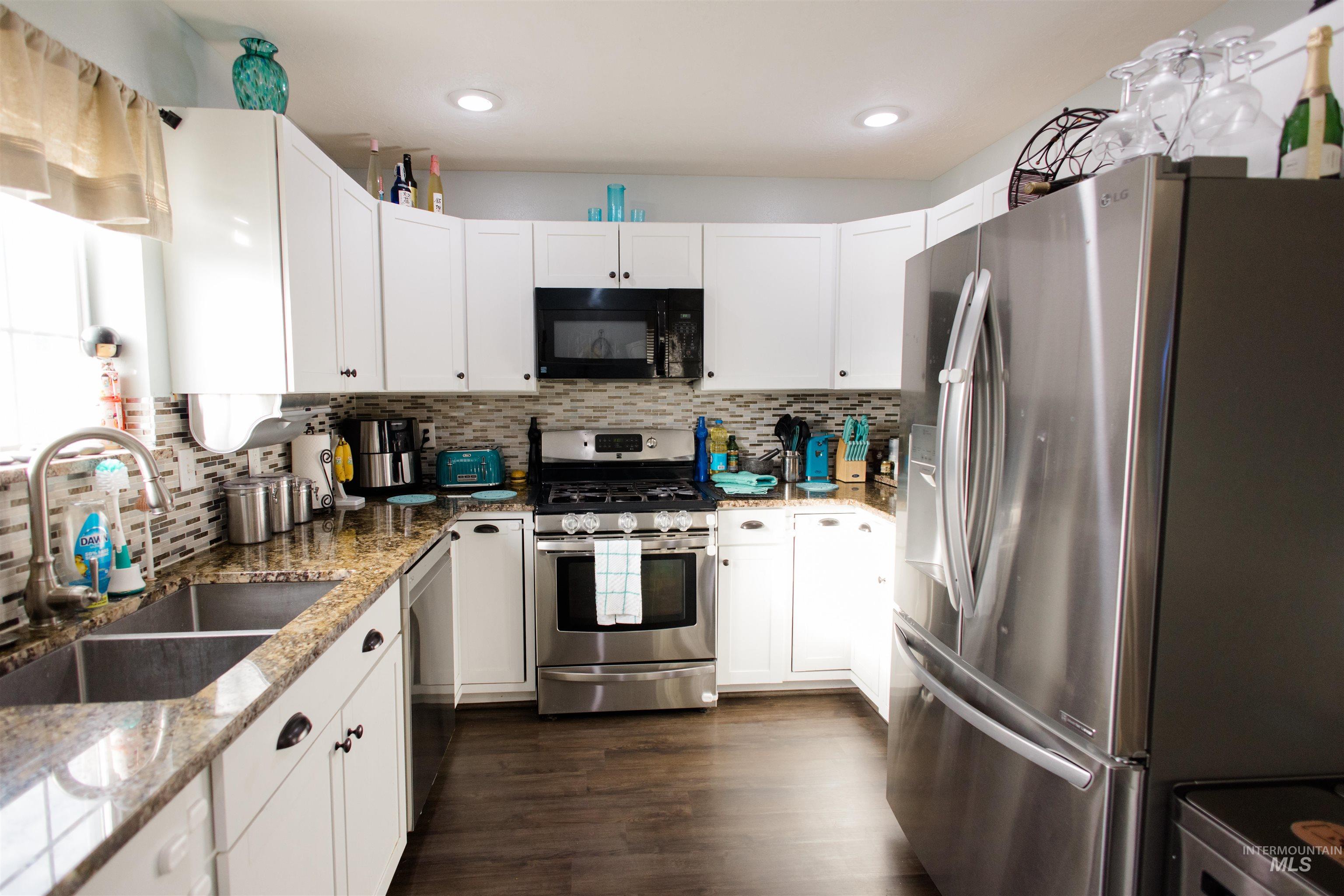 Kitchen featuring appliances with stainless steel finishes, white cabinets, light stone countertops, and dark wood-style floors
