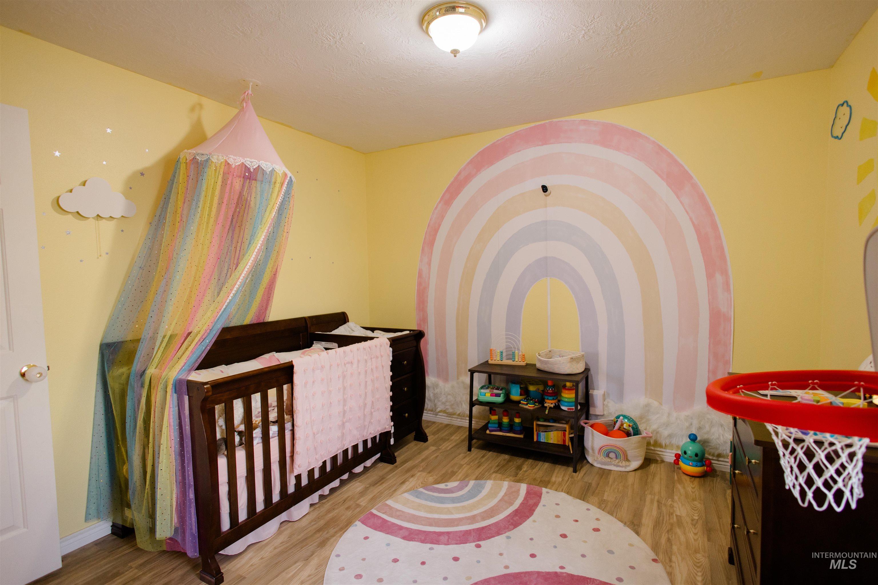 Bedroom featuring a nursery area, wood finished floors, and a textured ceiling