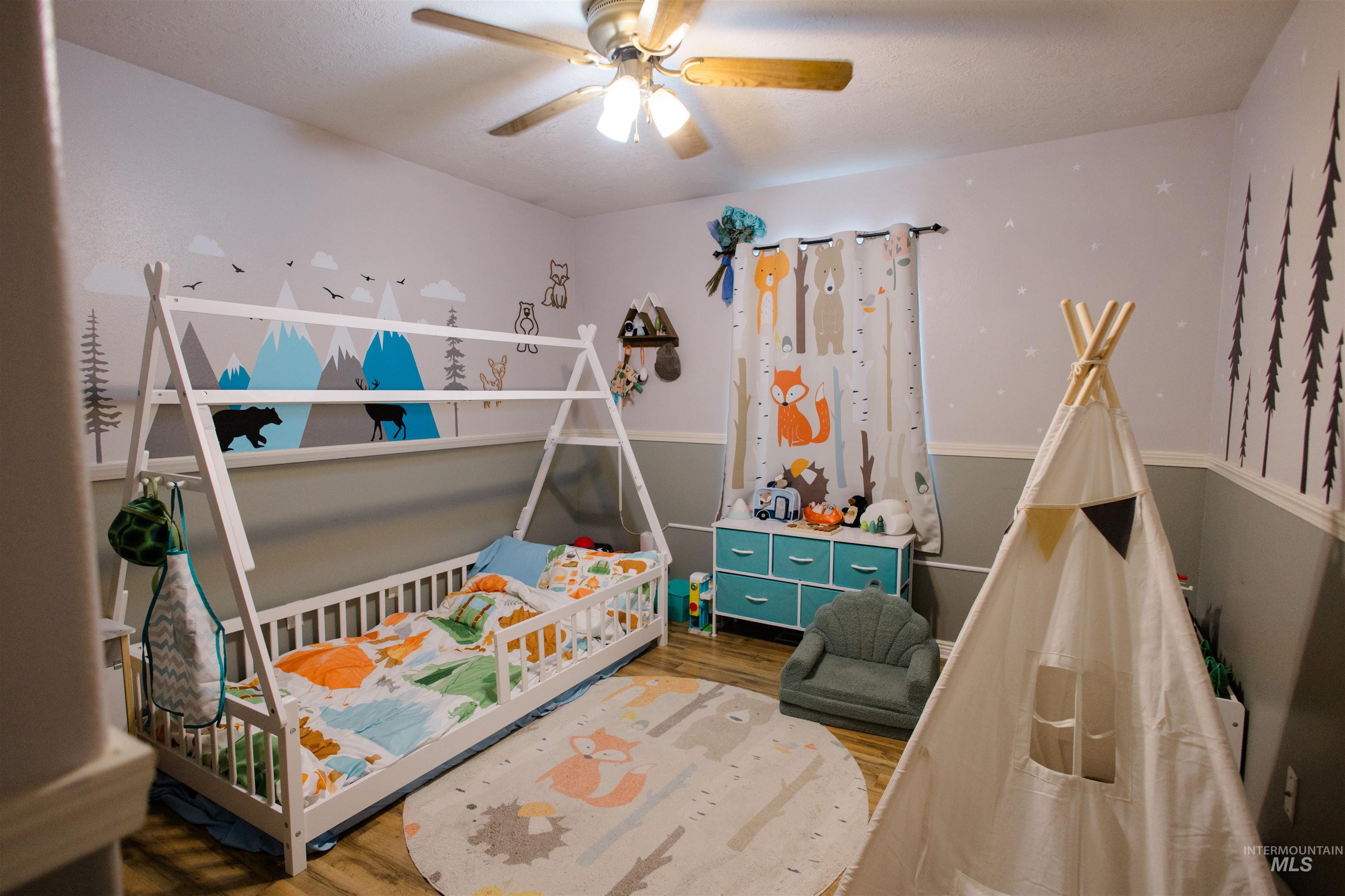 Bedroom with wood finished floors, ceiling fan, and a crib