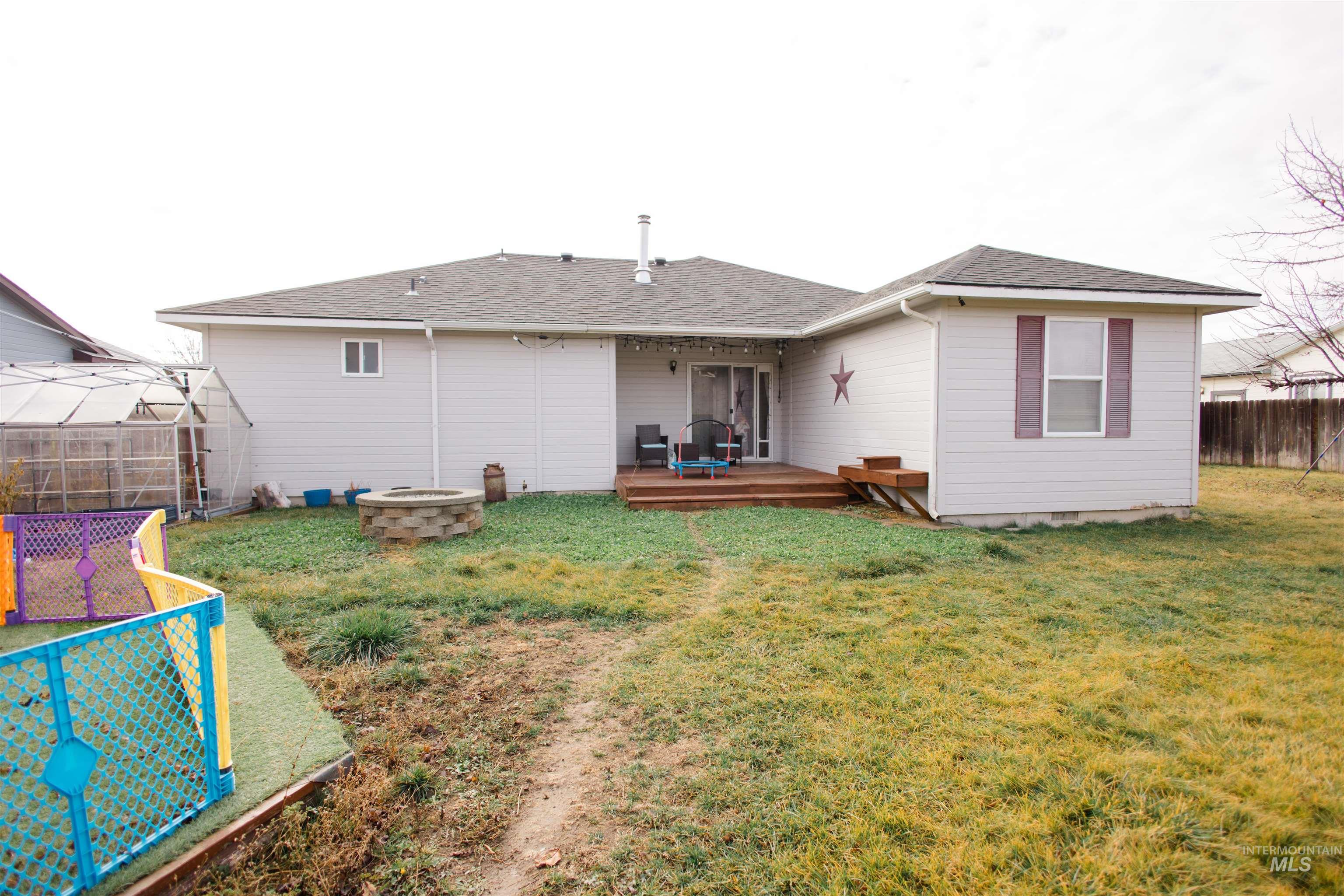 Back of house featuring a fenced backyard, roof with shingles, a fire pit, and a deck