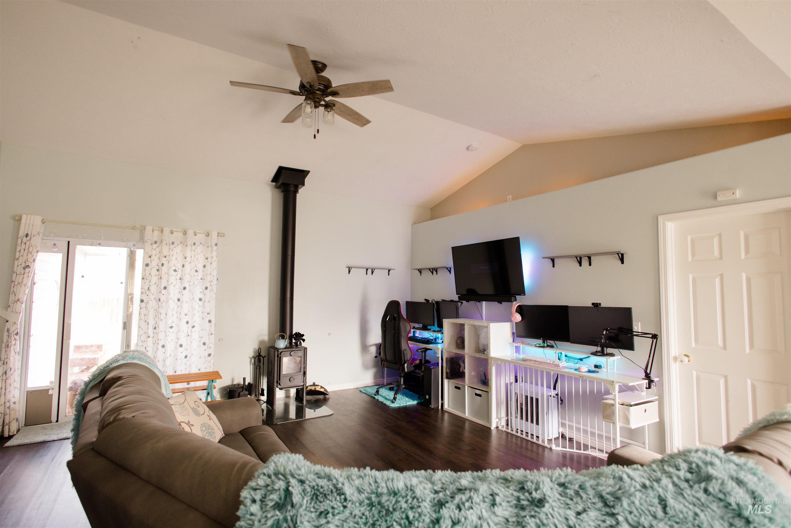 Living room with a wood stove, vaulted ceiling, wood finished floors, and a ceiling fan
