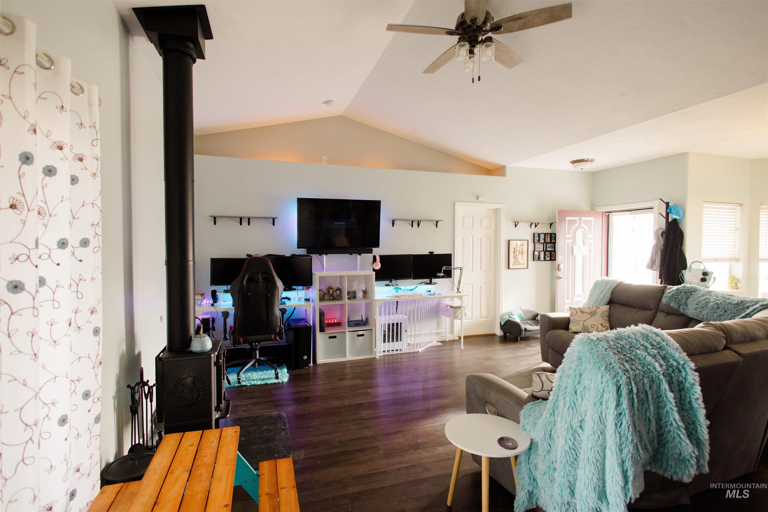 Living area with vaulted ceiling, wood finished floors, a wood stove, and ceiling fan