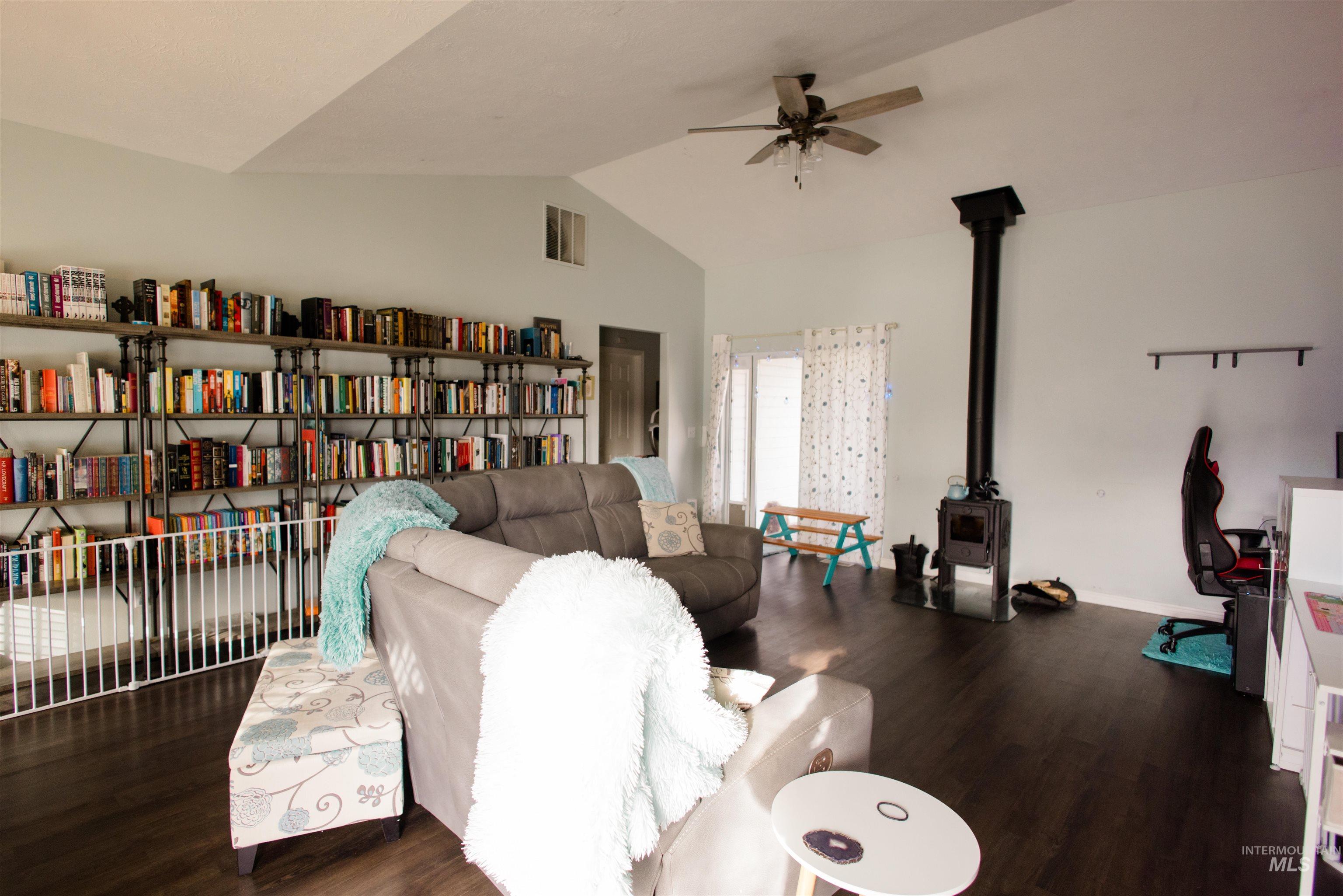 Living area featuring a wood stove, dark wood-style floors, lofted ceiling, and a ceiling fan