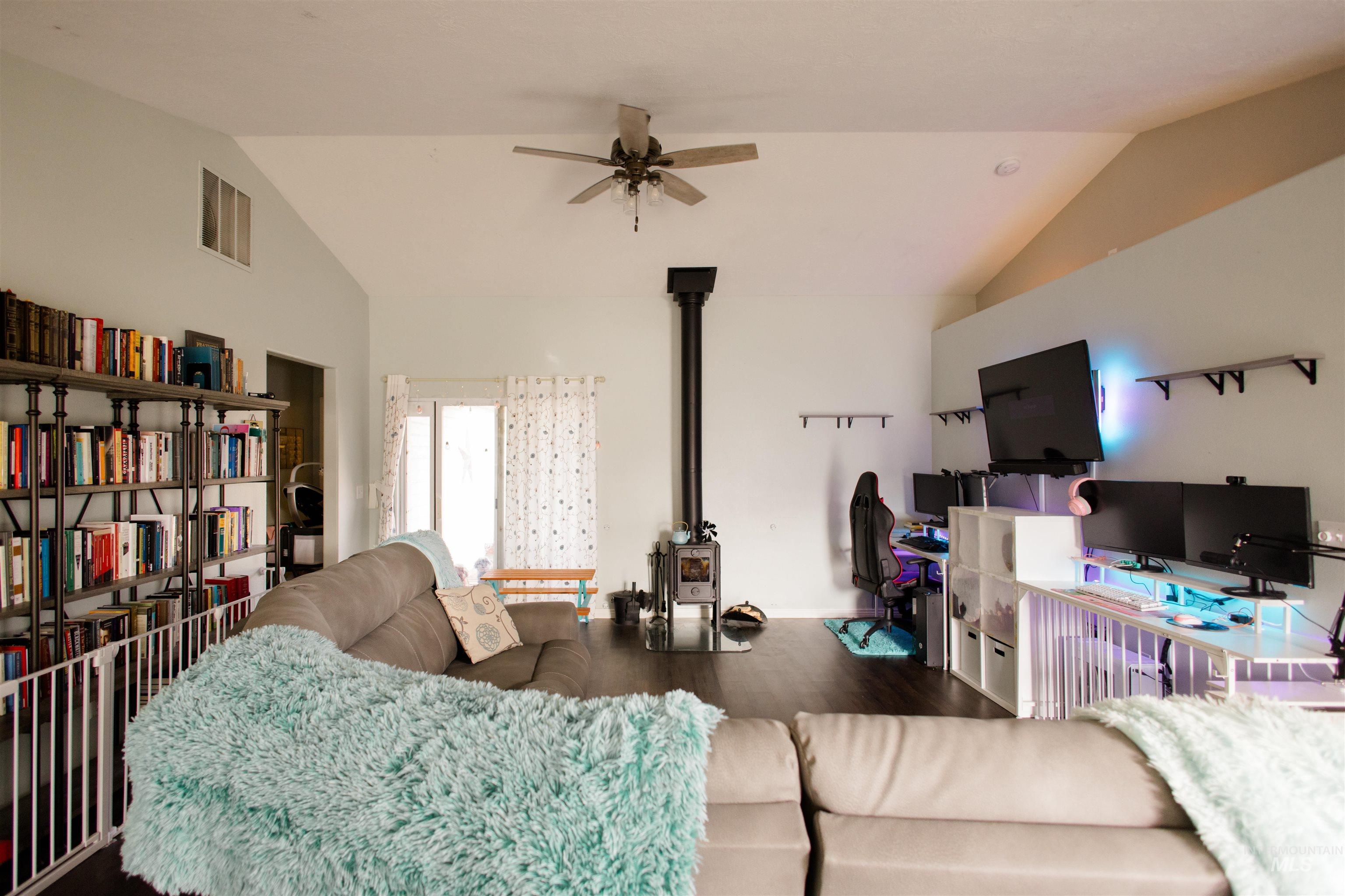 Living room featuring vaulted ceiling, wood finished floors, a wood stove, and a ceiling fan