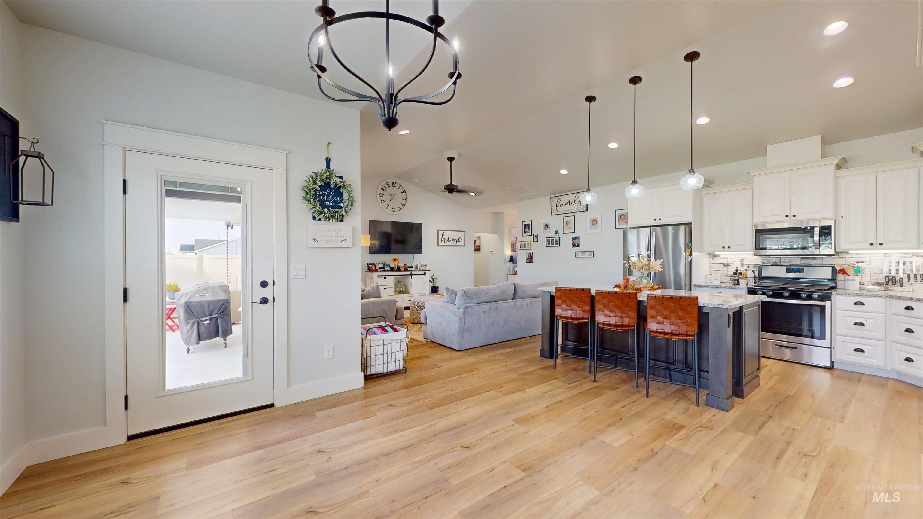 Kitchen featuring open floor plan, white cabinets, stainless steel appliances, decorative light fixtures, and decorative backsplash