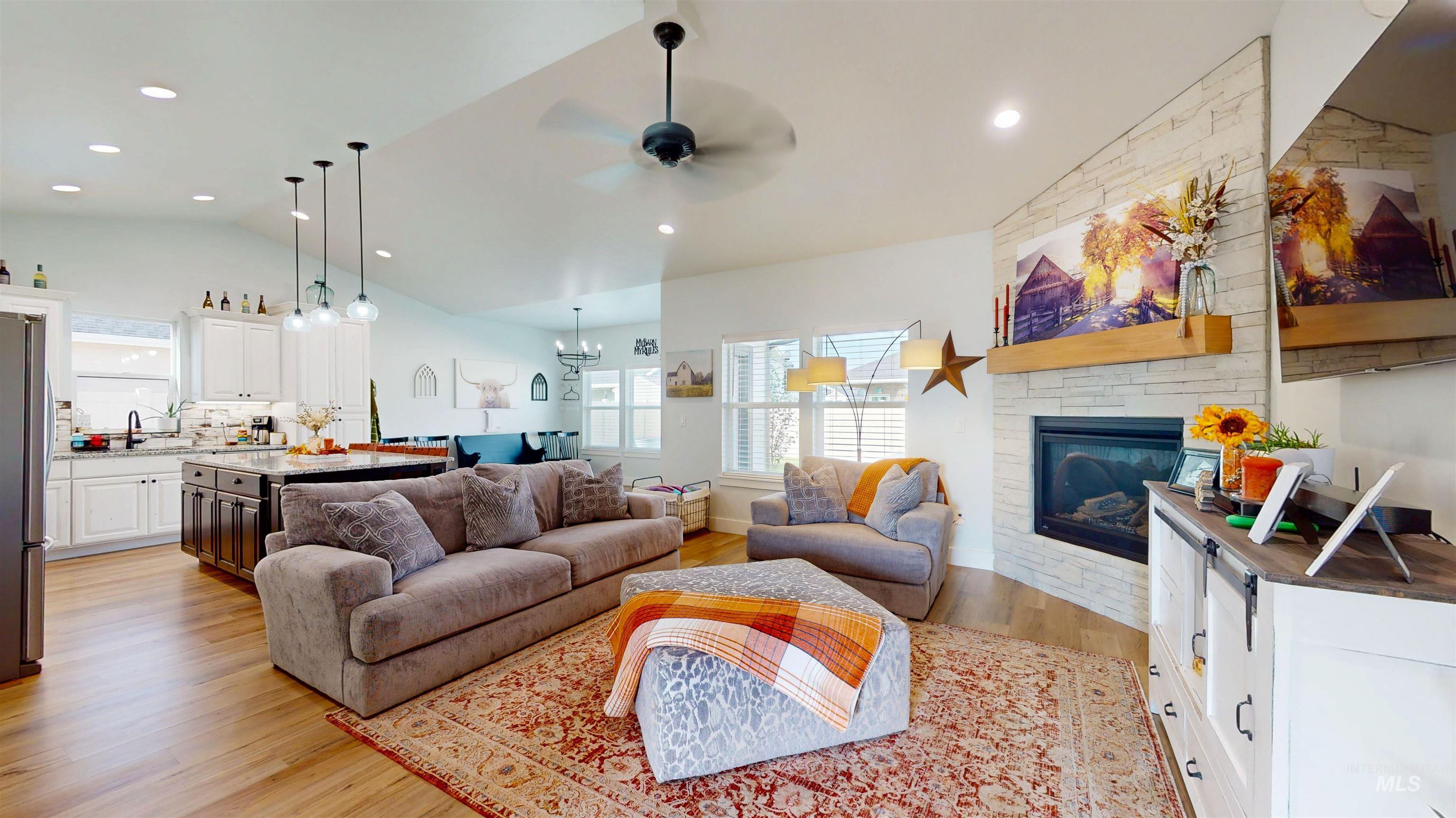 Living area featuring light wood-type flooring, lofted ceiling, ceiling fan, a stone fireplace, and recessed lighting