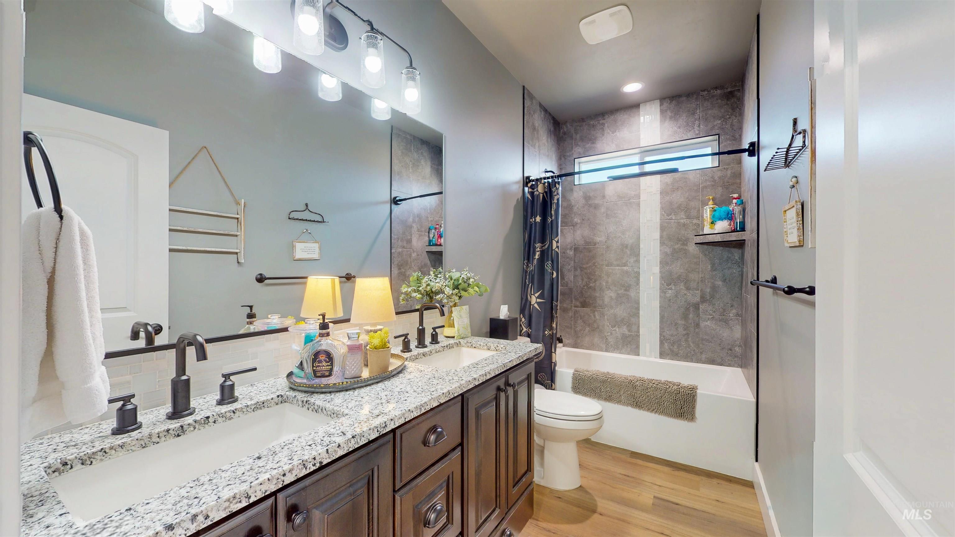 Bathroom with shower / bath combo with shower curtain, light wood finished floors, and double vanity