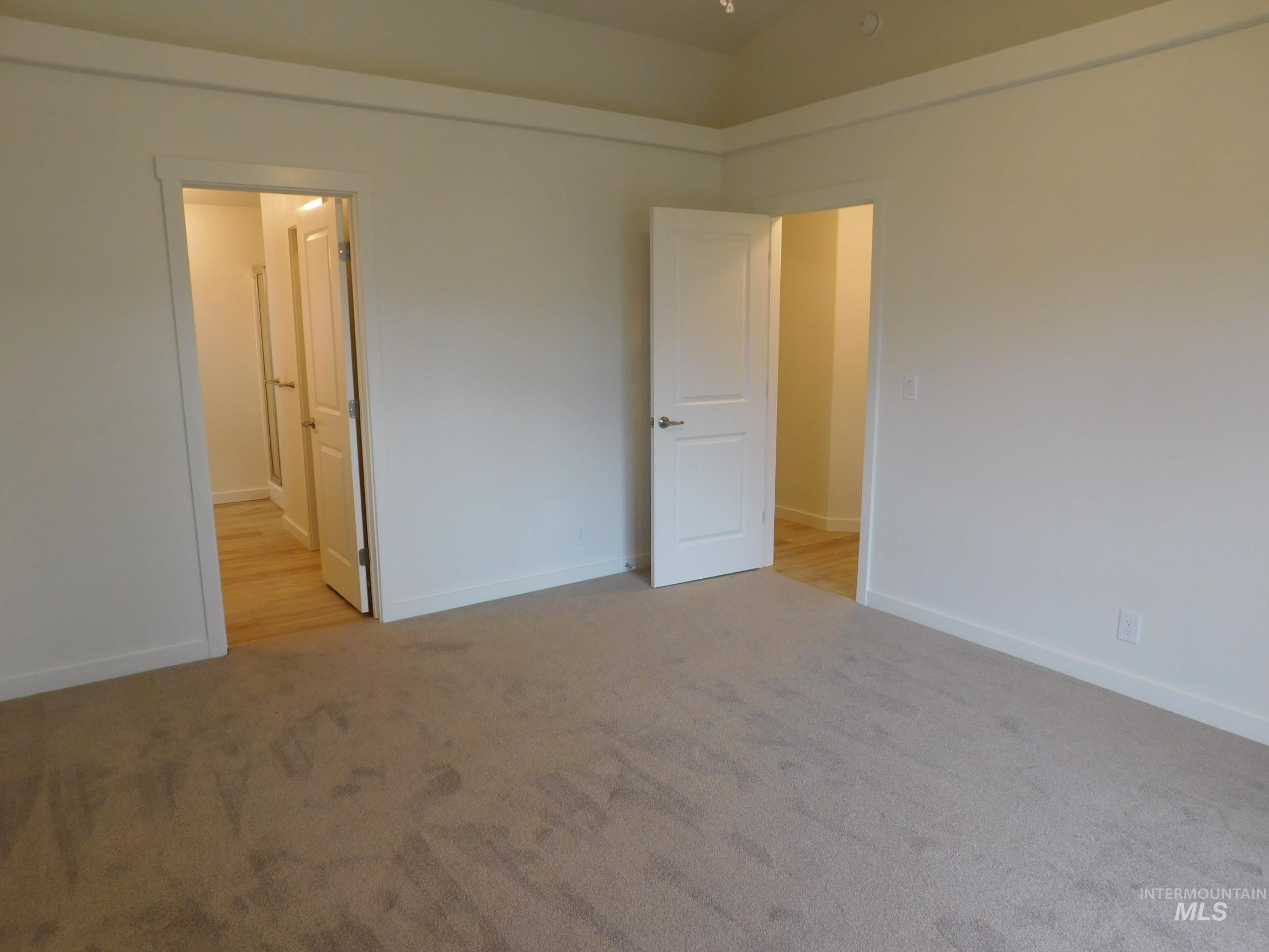 Unfurnished bedroom with light carpet, ensuite bathroom, and lofted ceiling