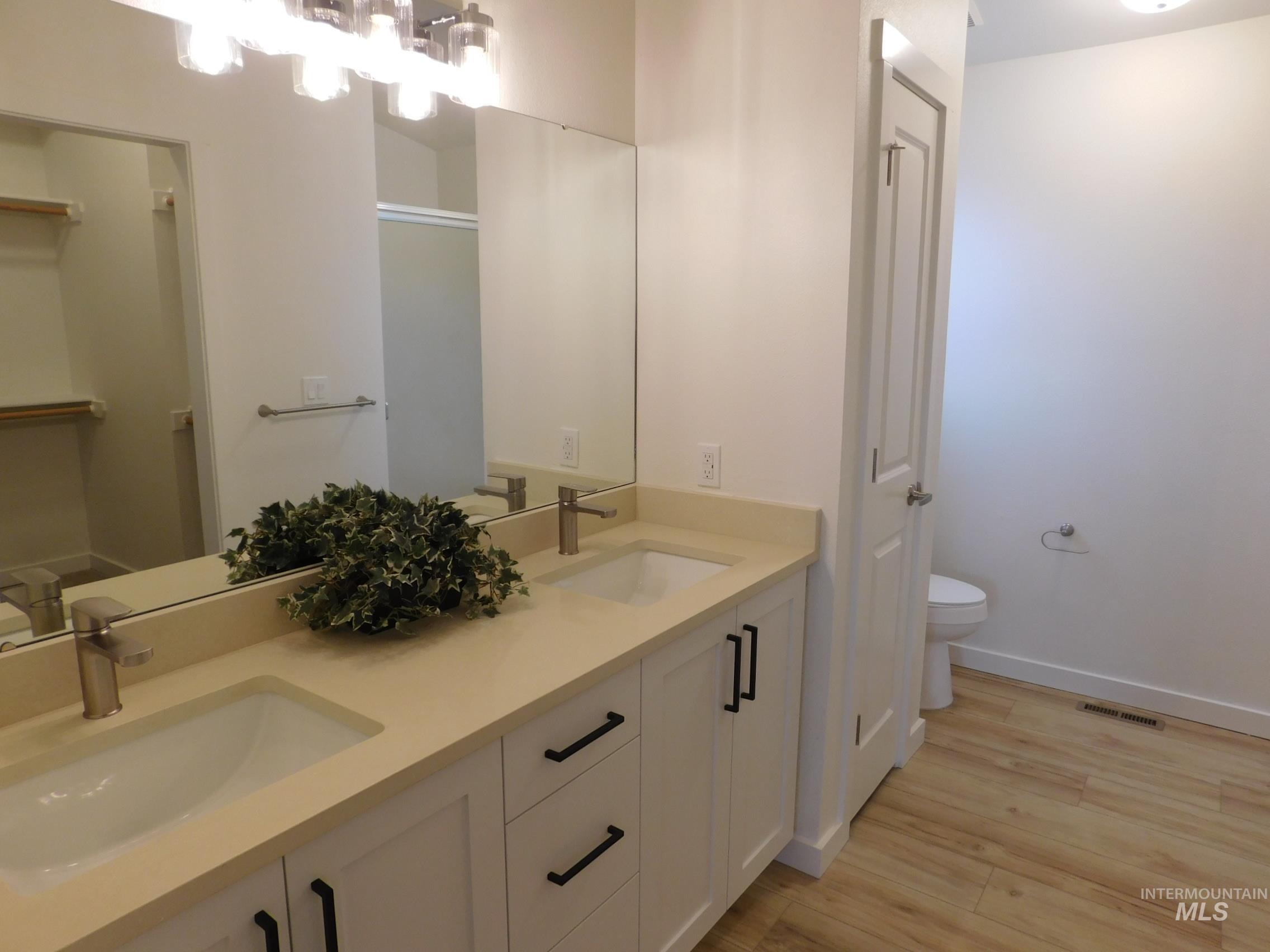 Full bathroom featuring double vanity, light wood-type flooring, and a stall shower