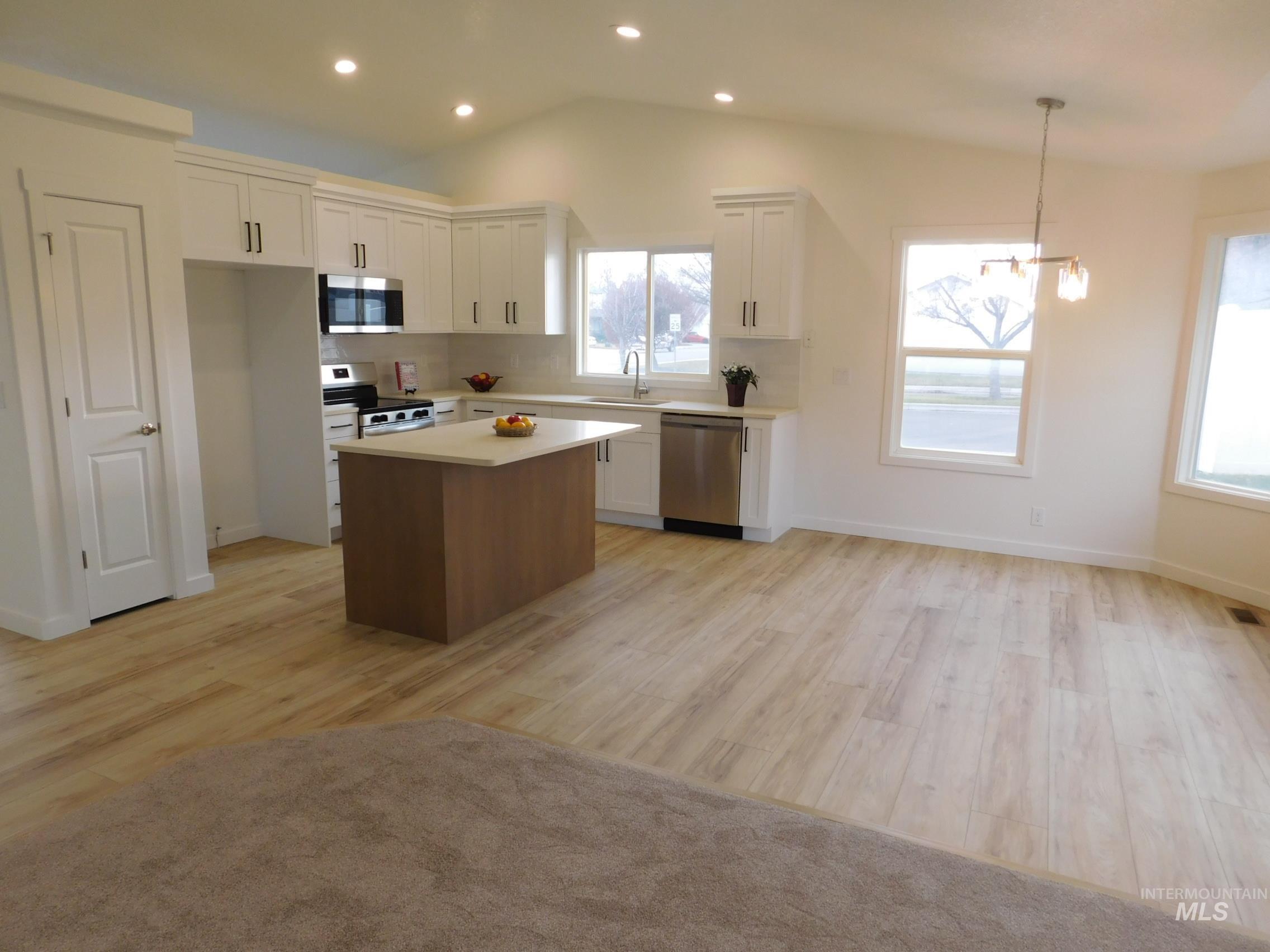 Kitchen featuring white cabinetry, a kitchen island, stainless steel appliances, vaulted ceiling, and light wood-style flooring