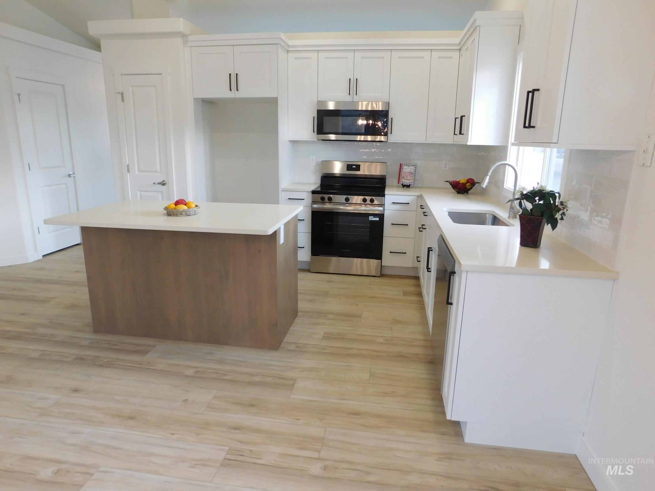 Kitchen with stainless steel appliances, white cabinetry, backsplash, a kitchen island, and light wood finished floors