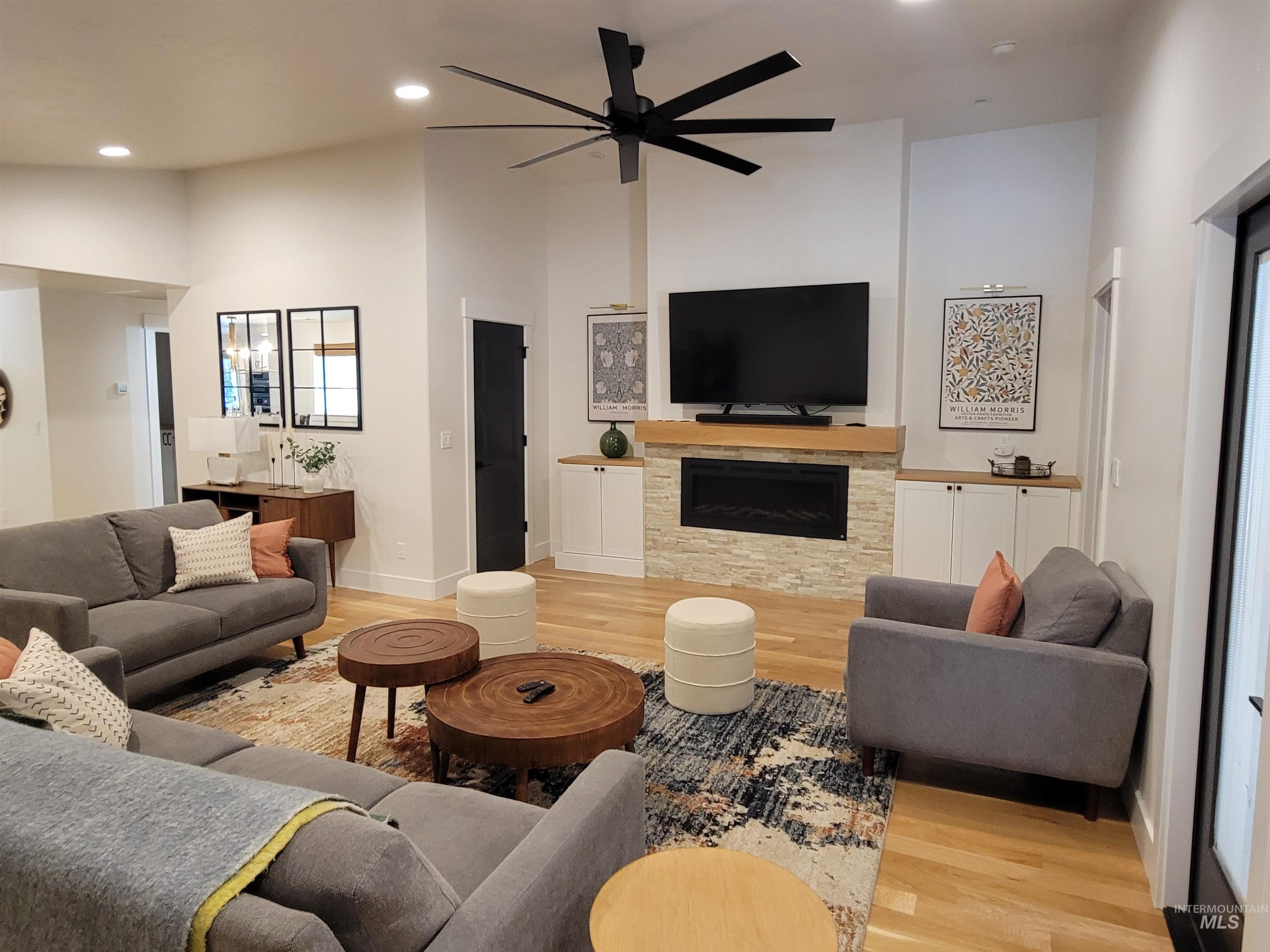Living area with light wood-type flooring, a high ceiling, a stone fireplace, recessed lighting, and a ceiling fan