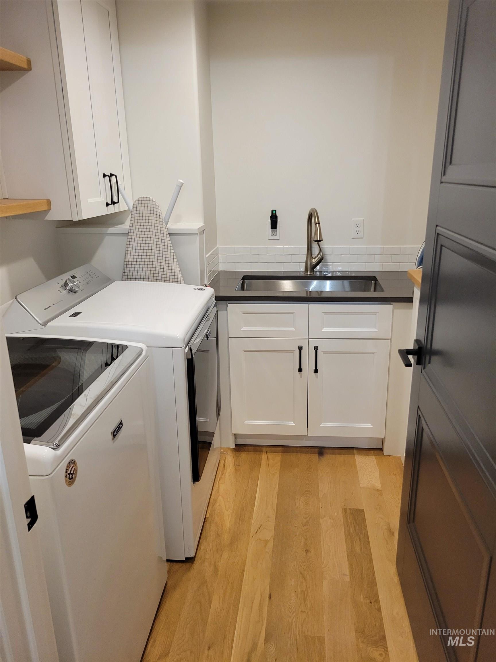 Laundry room with washing machine and dryer, light wood-type flooring, and cabinet space