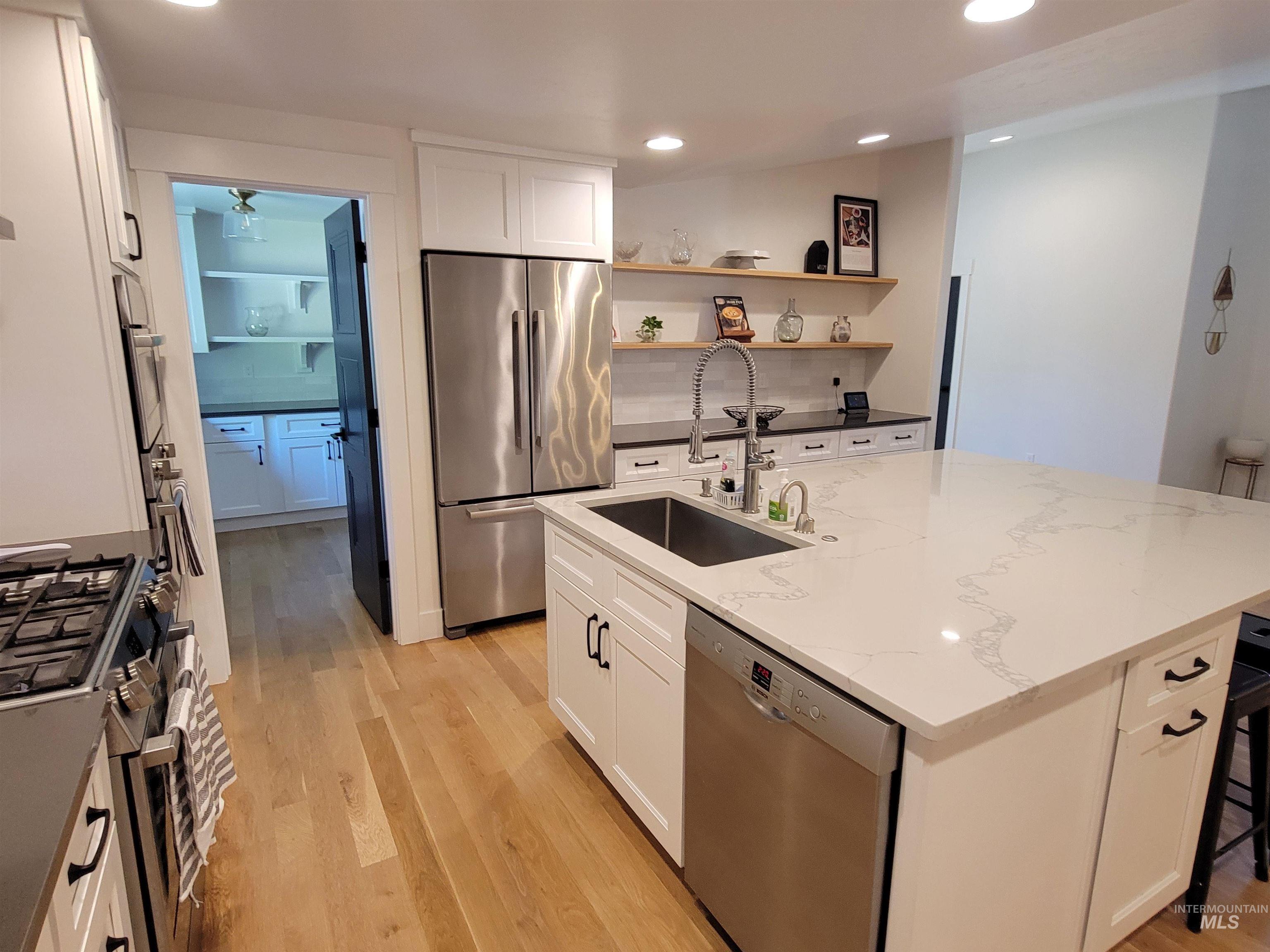 Kitchen featuring stainless steel appliances, light wood-style flooring, white cabinets, light stone countertops, and a center island with sink