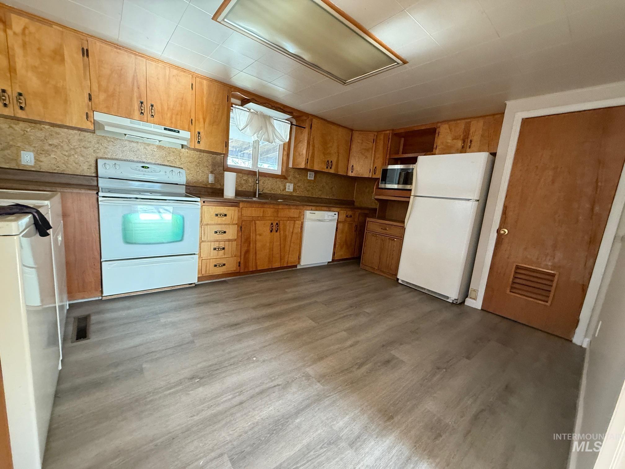 Kitchen featuring white appliances, under cabinet range hood, light wood-type flooring, tasteful backsplash, and brown cabinets