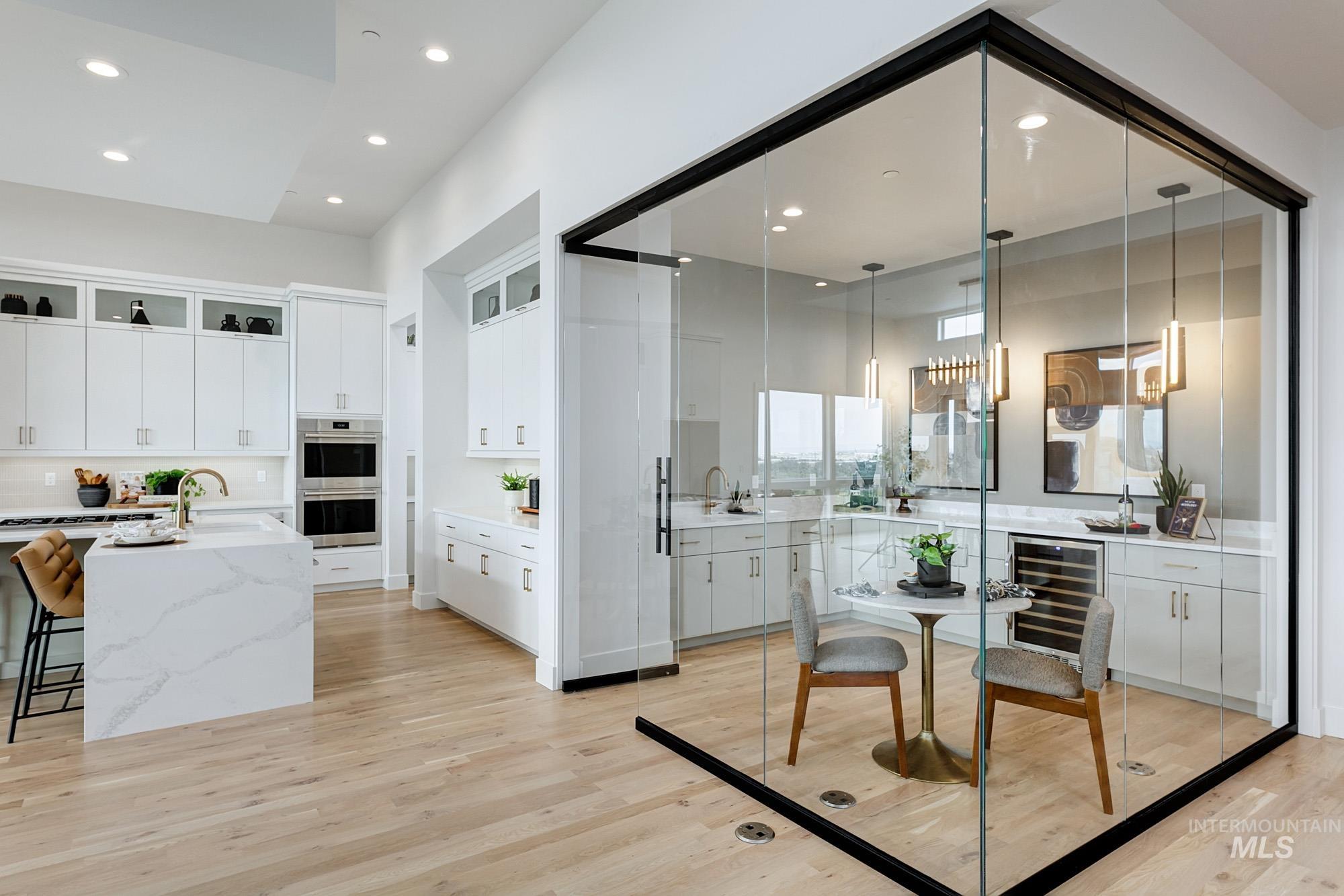Kitchen with white cabinets, light stone countertops, beverage cooler, hanging light fixtures, and light wood-style flooring