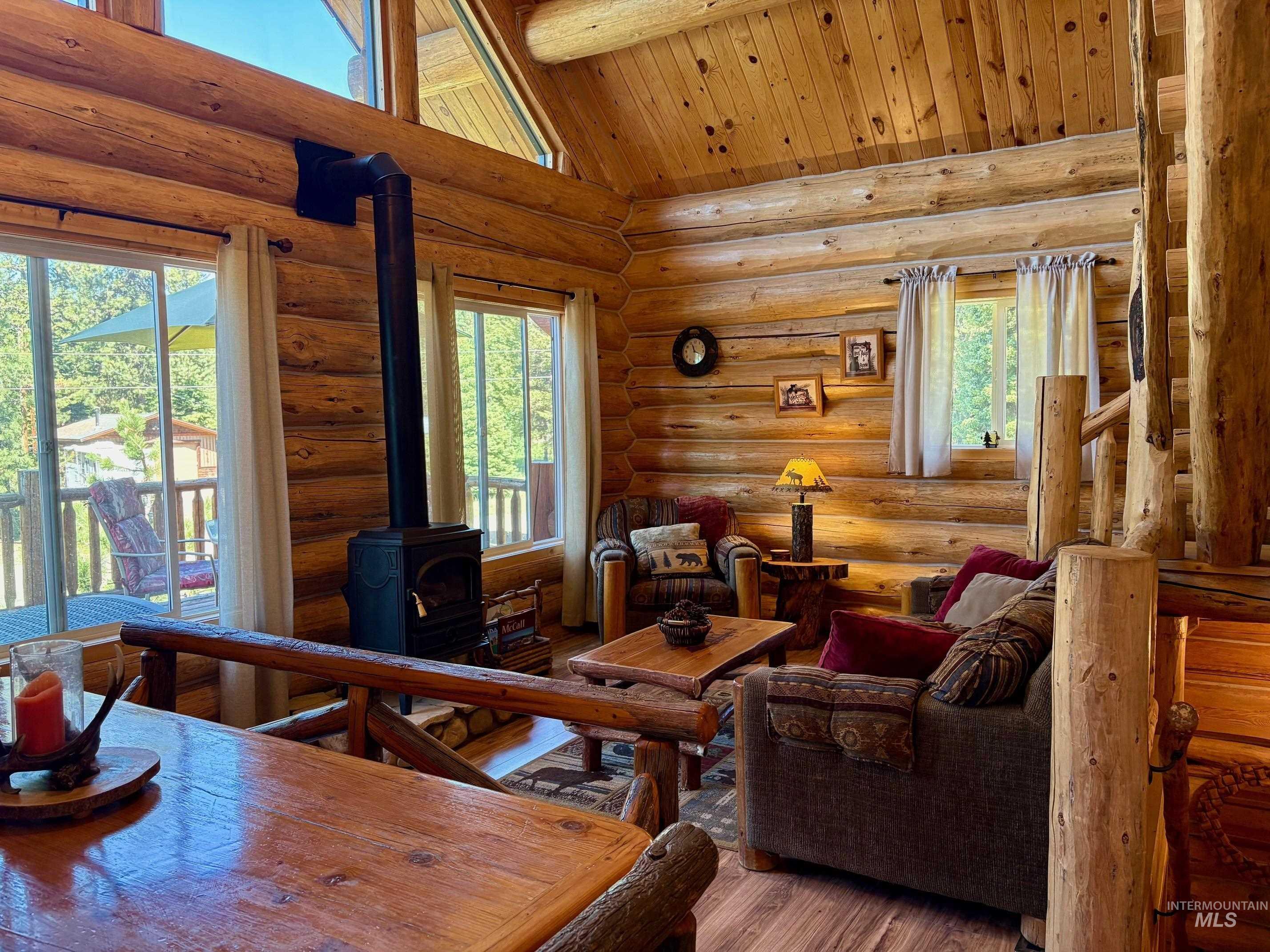 Living room with a wood stove, log walls, hardwood / wood-style floors, high vaulted ceiling, and a wooden ceiling with exposed beams
