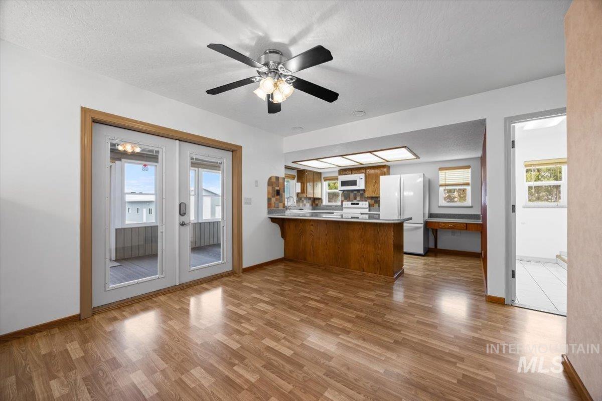 Kitchen with brown cabinets, a textured ceiling, white appliances, a peninsula, and dark wood-style flooring