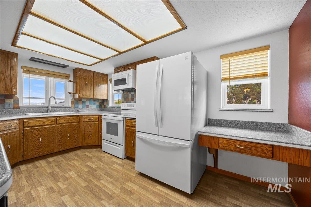 Kitchen with white appliances, brown cabinets, light countertops, light wood finished floors, and tasteful backsplash