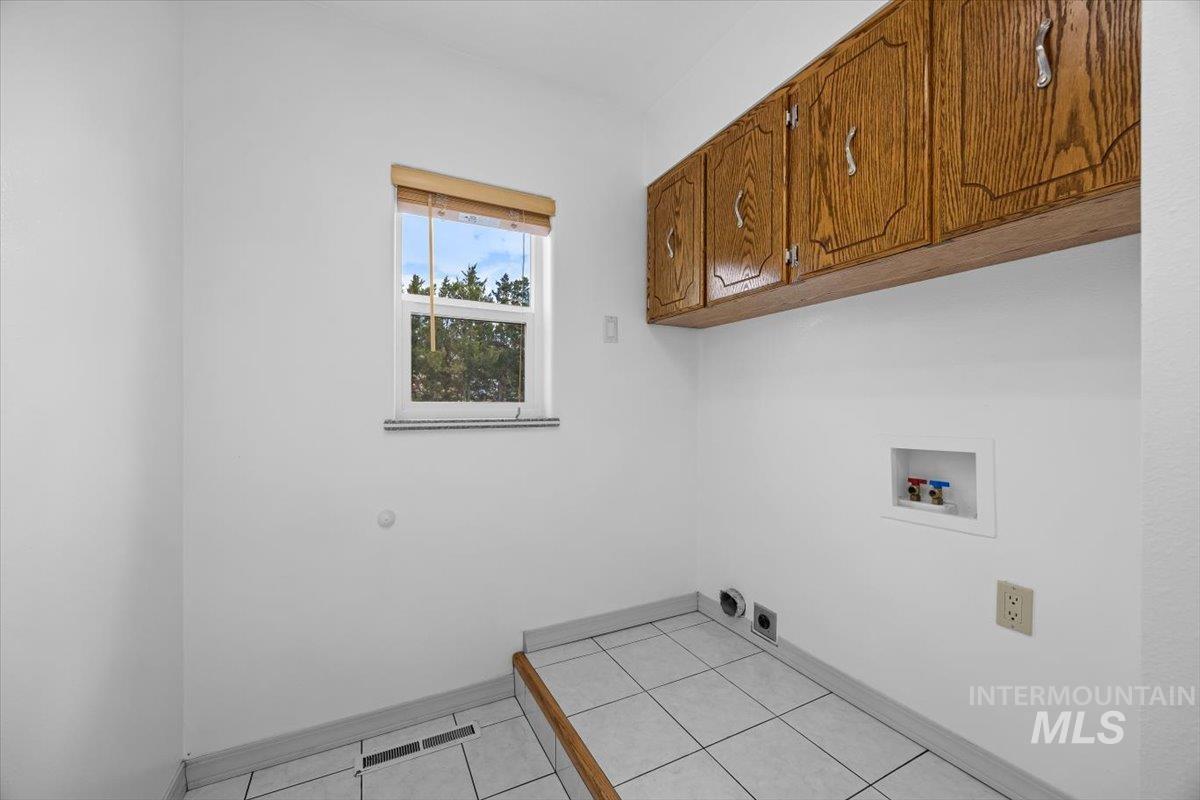 Washroom with cabinet space, washer hookup, light tile patterned floors, and hookup for an electric dryer