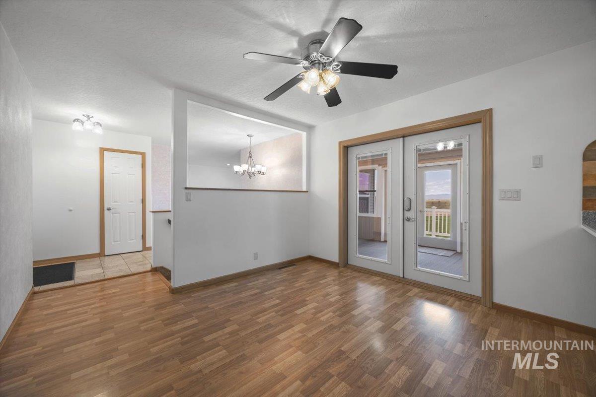 Unfurnished room featuring wood finished floors, a chandelier, a textured ceiling, ceiling fan, and french doors