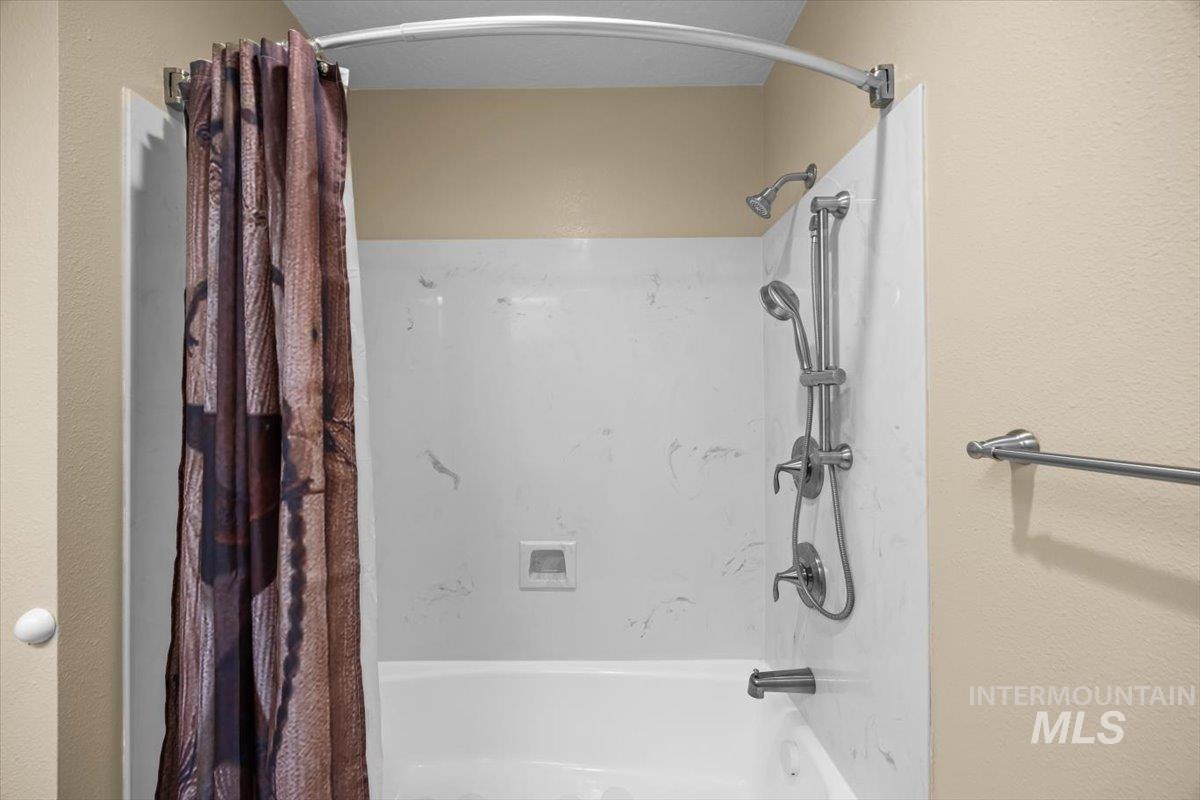 Bathroom featuring shower / bathtub combination with curtain and a textured wall