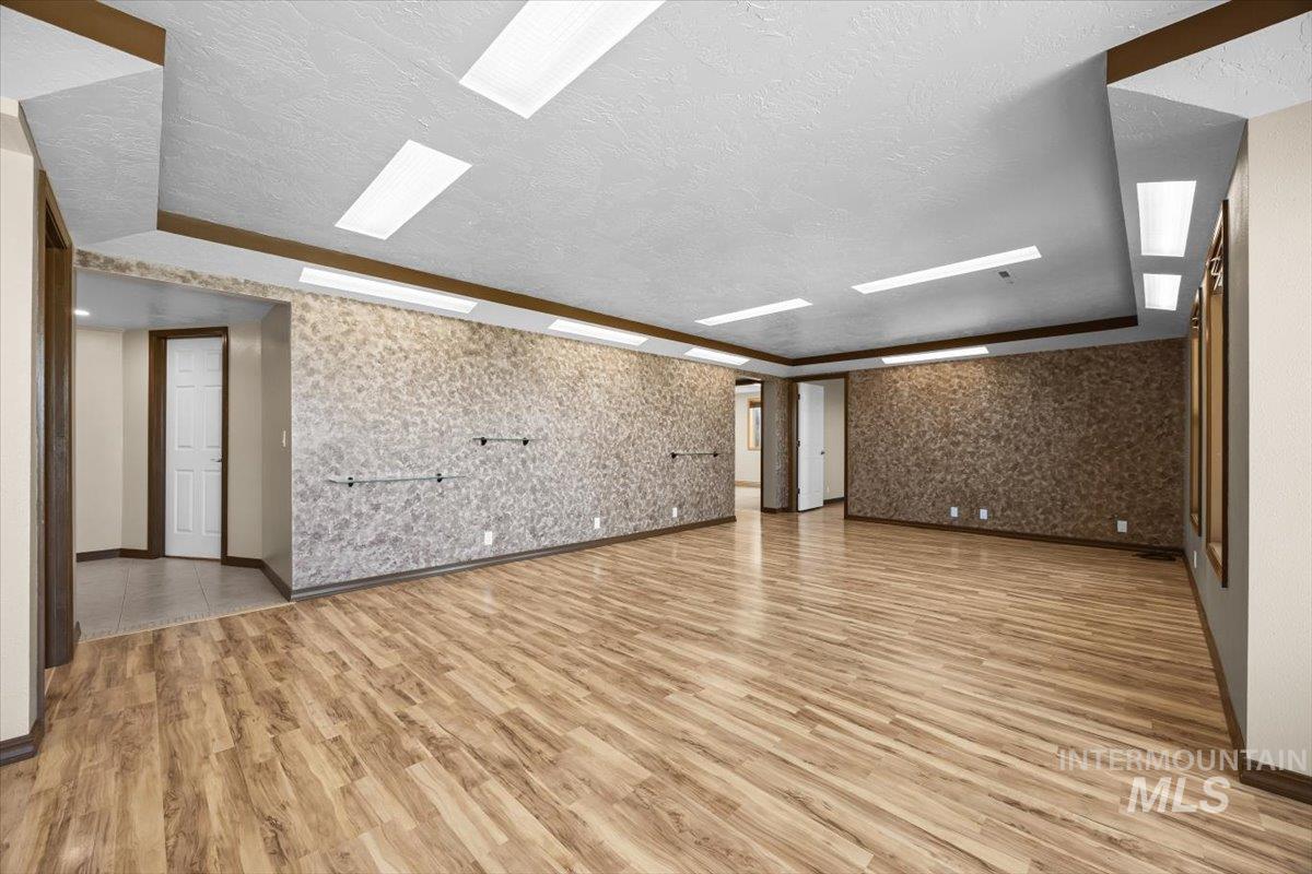 Empty room with a textured ceiling, light wood-style flooring, an accent wall, and wallpapered walls