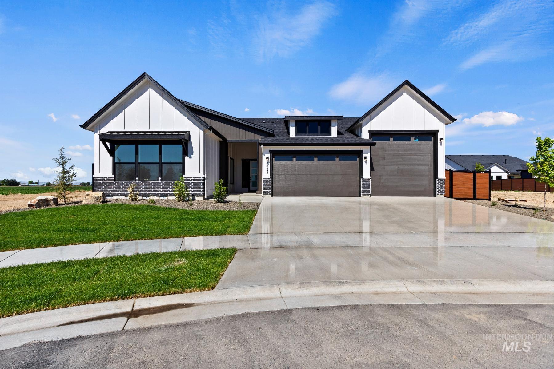 Modern inspired farmhouse featuring board and batten siding, driveway, a front lawn, a garage, and stone siding