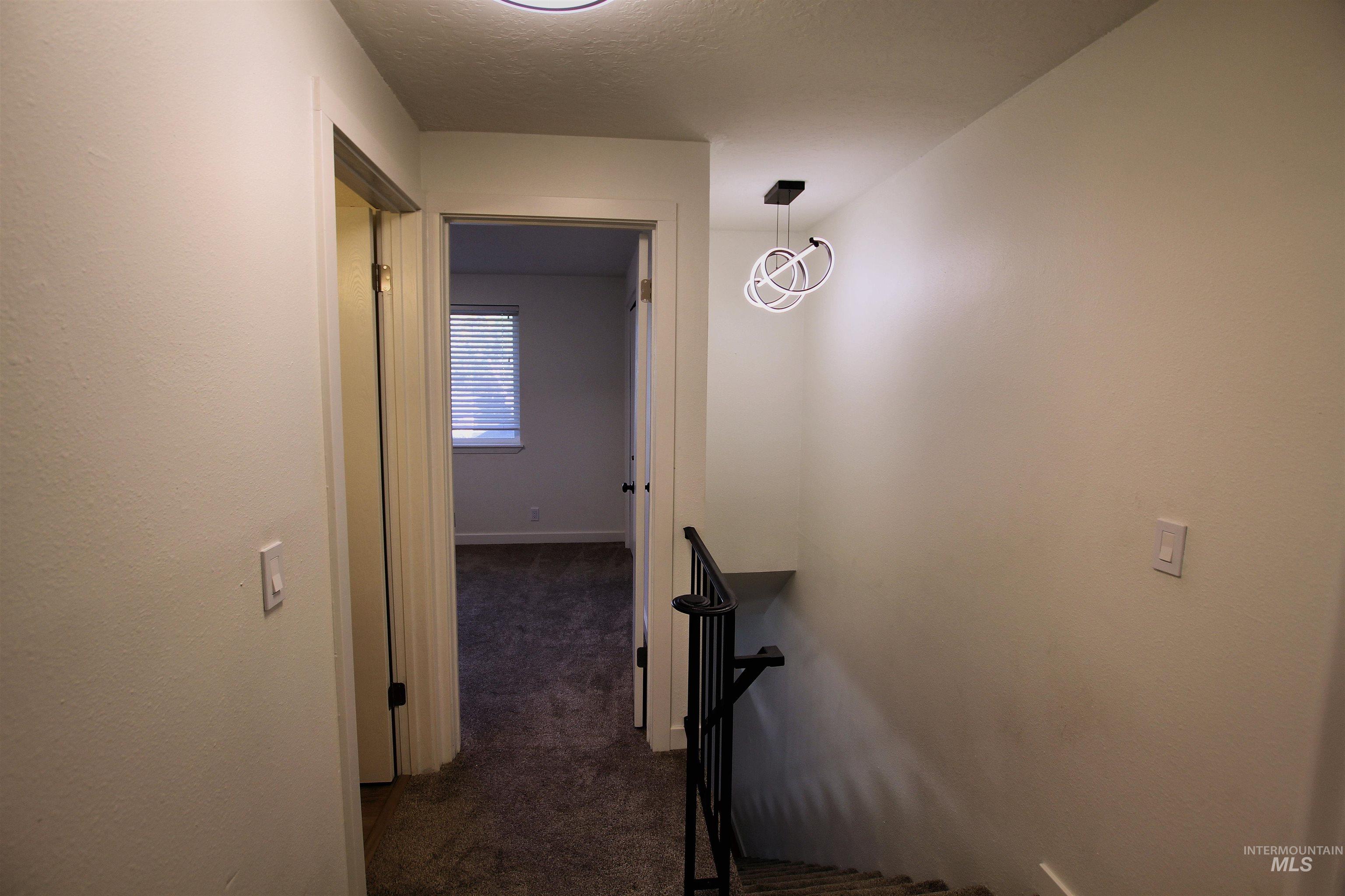 Corridor featuring dark colored carpet, a textured ceiling, and an upstairs landing