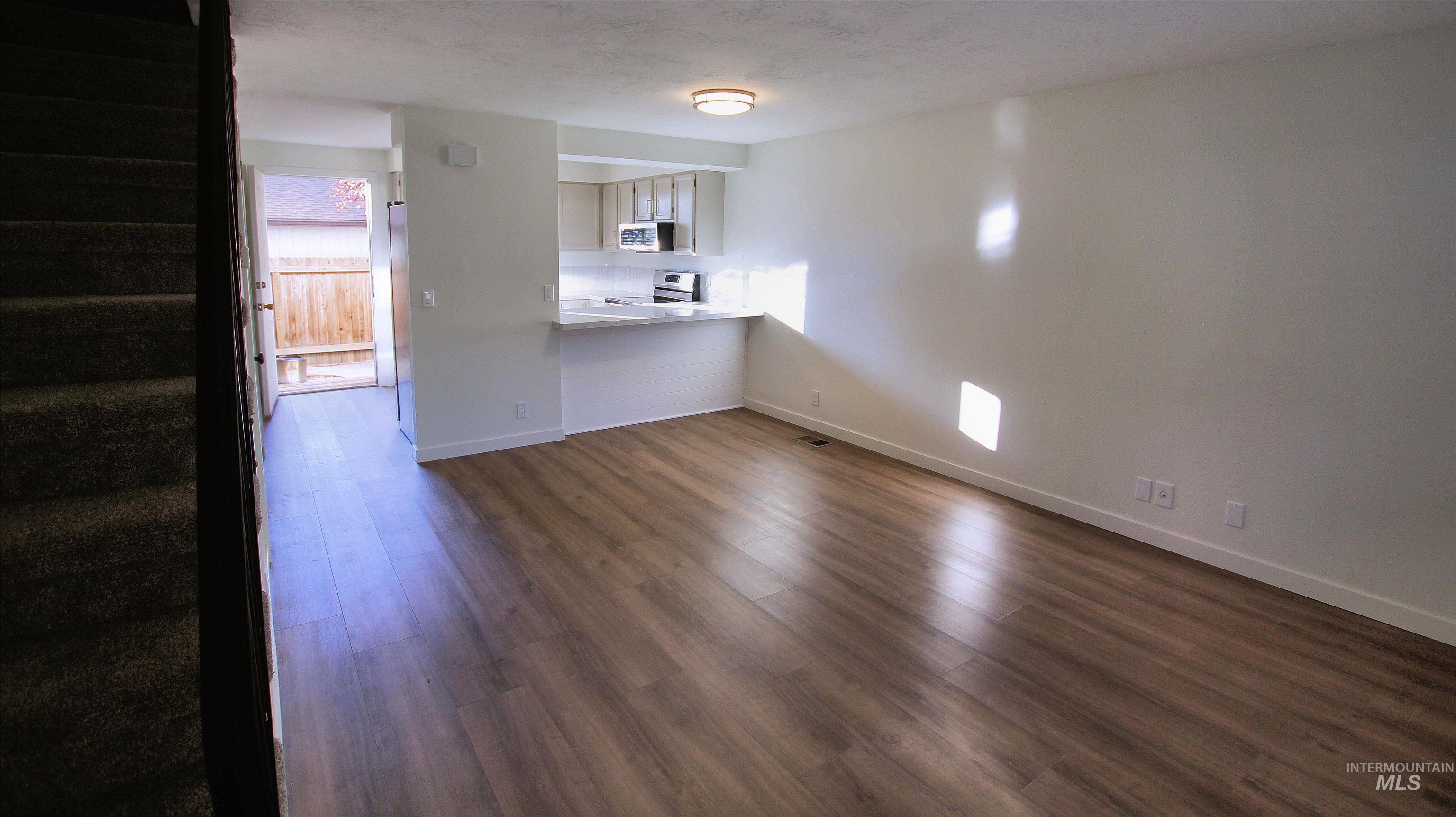 Unfurnished living room with stairs, dark wood finished floors, and a textured ceiling