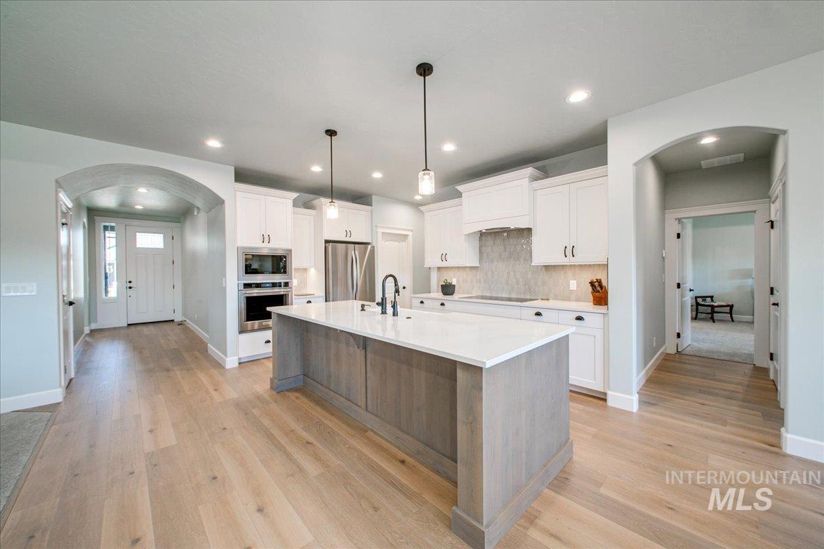 Kitchen featuring arched walkways, white cabinets, appliances with stainless steel finishes, an island with sink, and recessed lighting