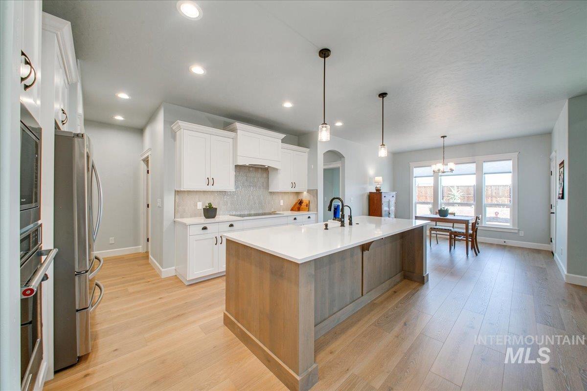 Kitchen with white cabinets, backsplash, appliances with stainless steel finishes, hanging light fixtures, and a center island with sink