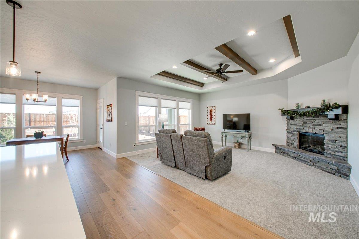 Living room with light wood finished floors, a raised ceiling, a fireplace, healthy amount of natural light, and beam ceiling
