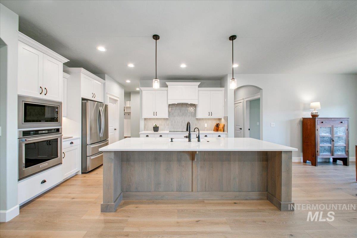 Kitchen with stainless steel appliances, white cabinetry, hanging light fixtures, arched walkways, and a large island