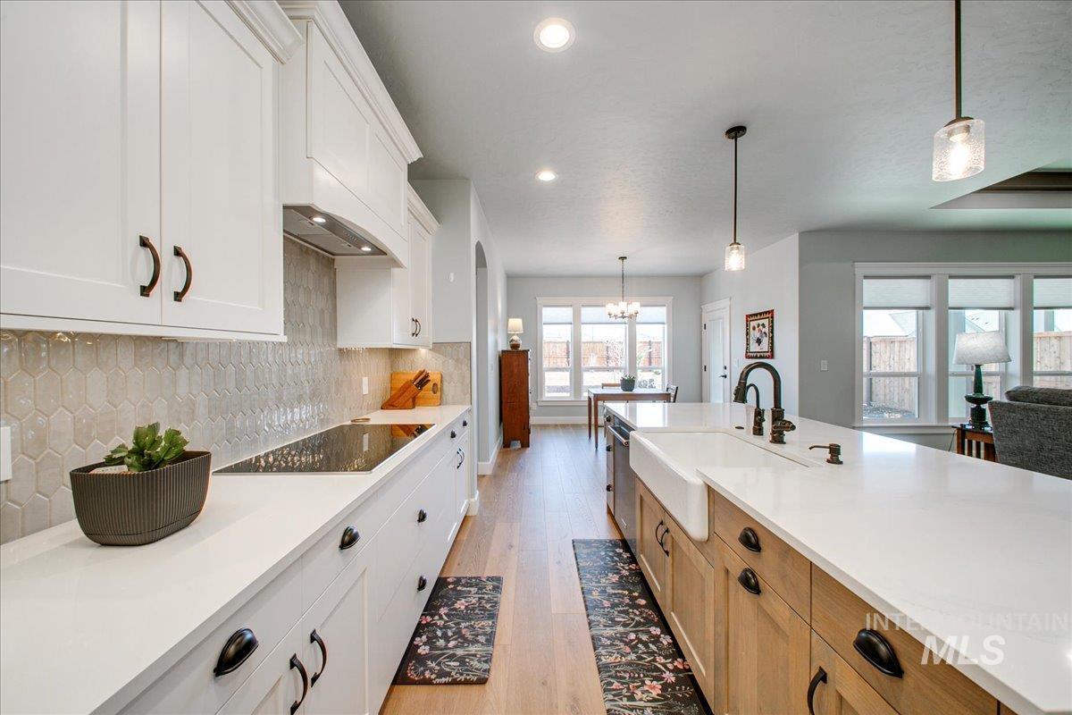 Kitchen with white cabinets, hanging light fixtures, light wood-style floors, backsplash, and recessed lighting