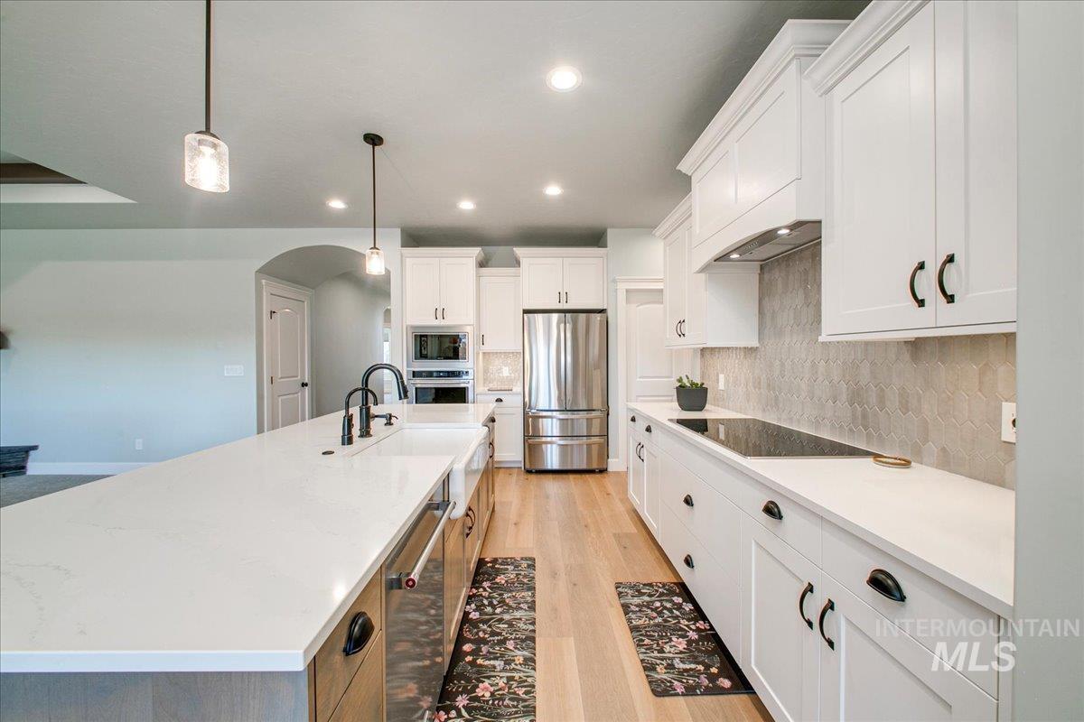 Kitchen featuring hanging light fixtures, stainless steel appliances, arched walkways, white cabinetry, and recessed lighting