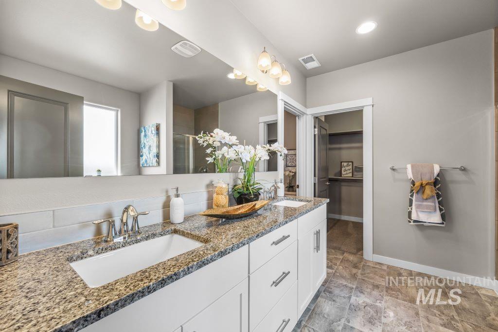 Bathroom with double vanity, a stall shower, stone finish floors, a walk in closet, and recessed lighting