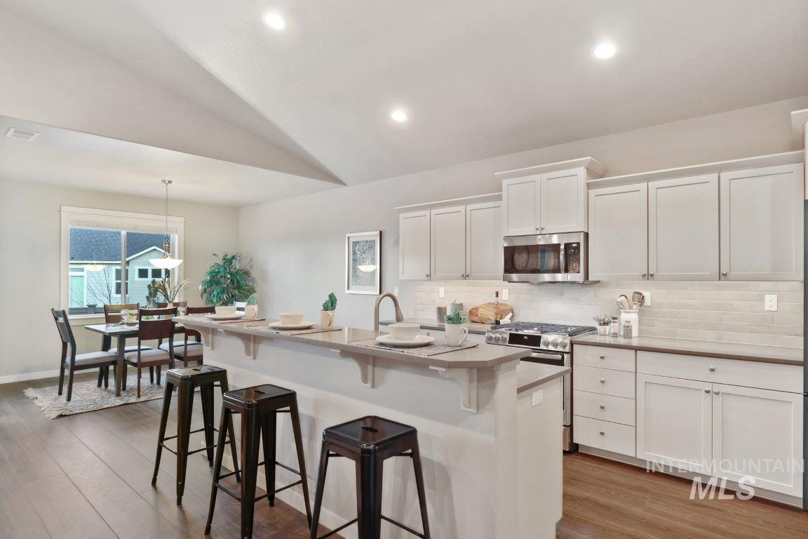 Kitchen featuring a kitchen bar, white cabinets, appliances with stainless steel finishes, tasteful backsplash, and hanging light fixtures
