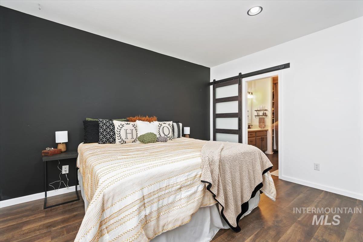 Bedroom featuring a barn door, dark wood-style flooring, ensuite bath, and recessed lighting