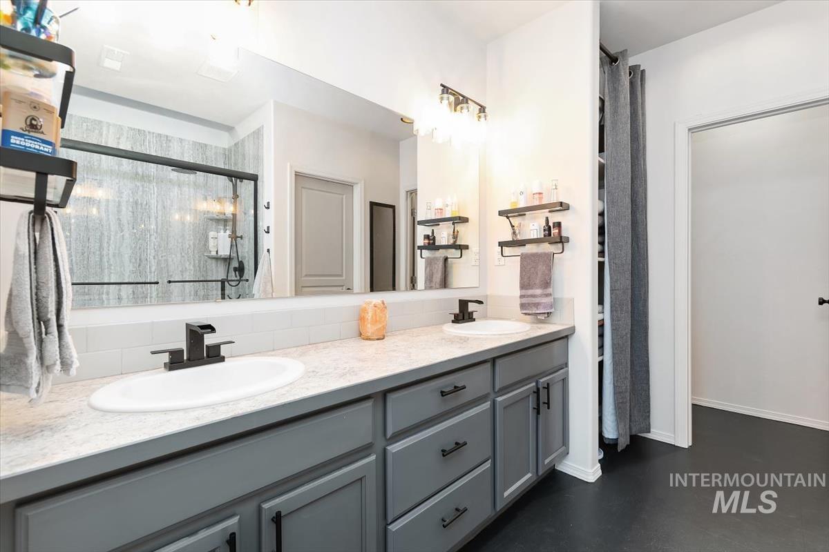 Full bath featuring double vanity, a shower stall, and finished concrete floors