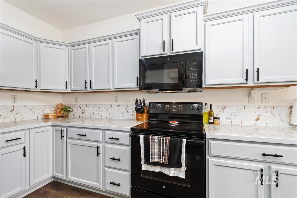 Kitchen featuring black appliances, white cabinets, light stone countertops, and dark wood-type flooring