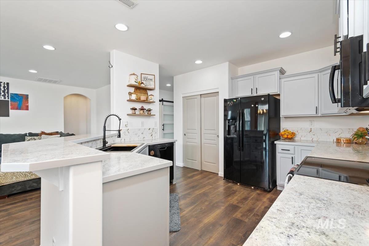 Kitchen featuring black appliances, recessed lighting, light stone counters, a barn door, and dark wood-style flooring