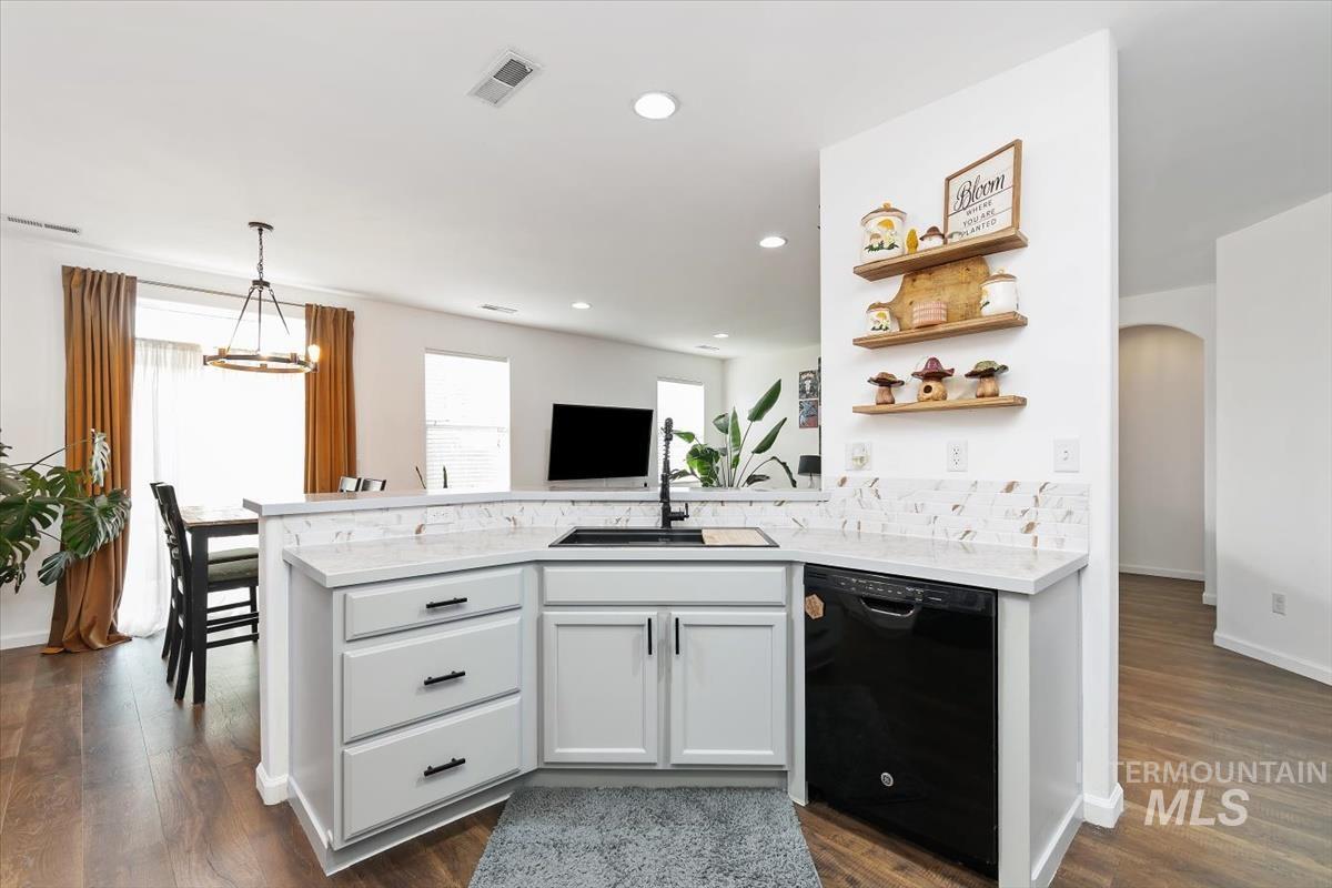 Kitchen featuring dishwasher, open shelves, arched walkways, hanging light fixtures, and a peninsula