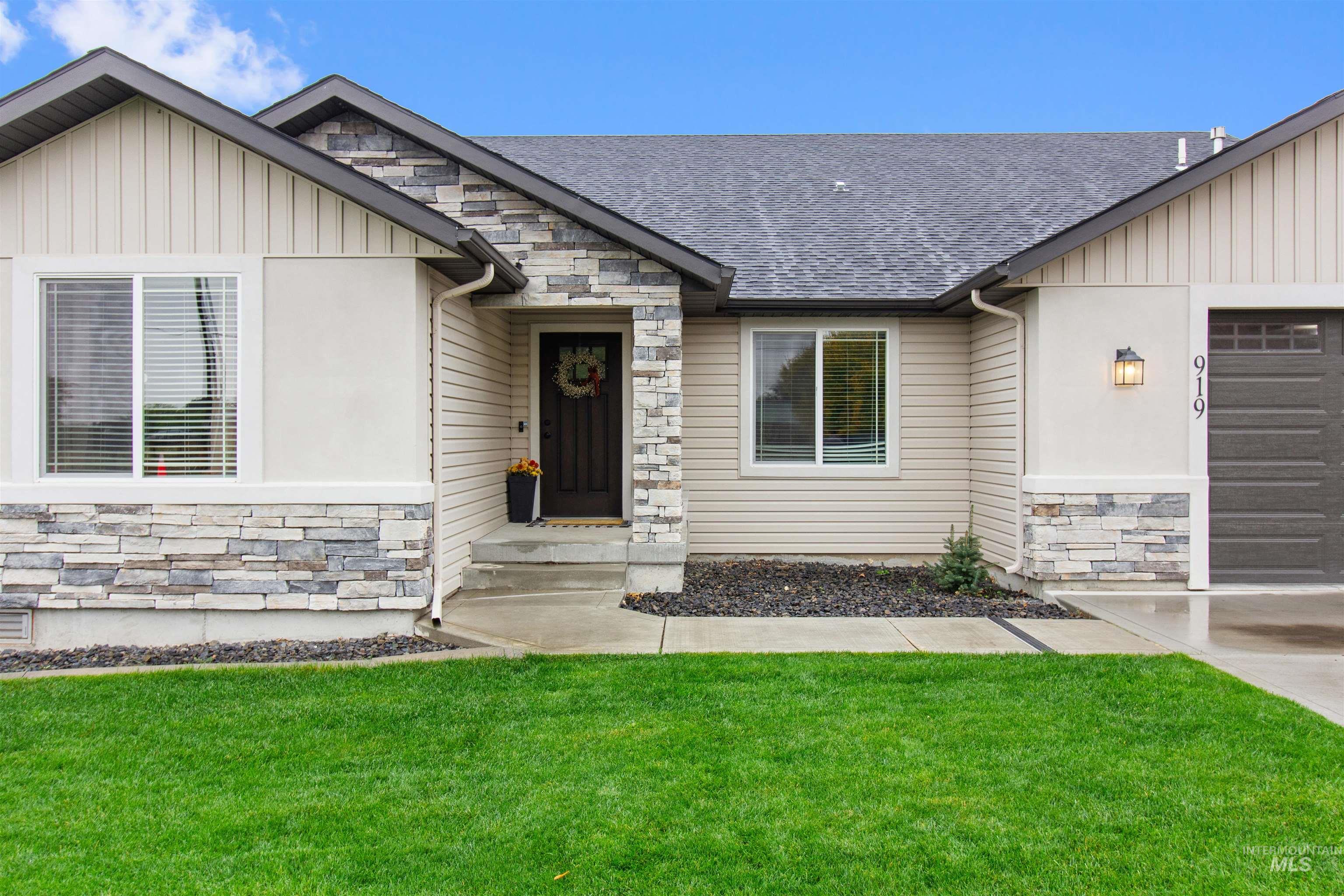 View of front of property with stone siding, a garage, a front yard, board and batten siding, and roof with shingles