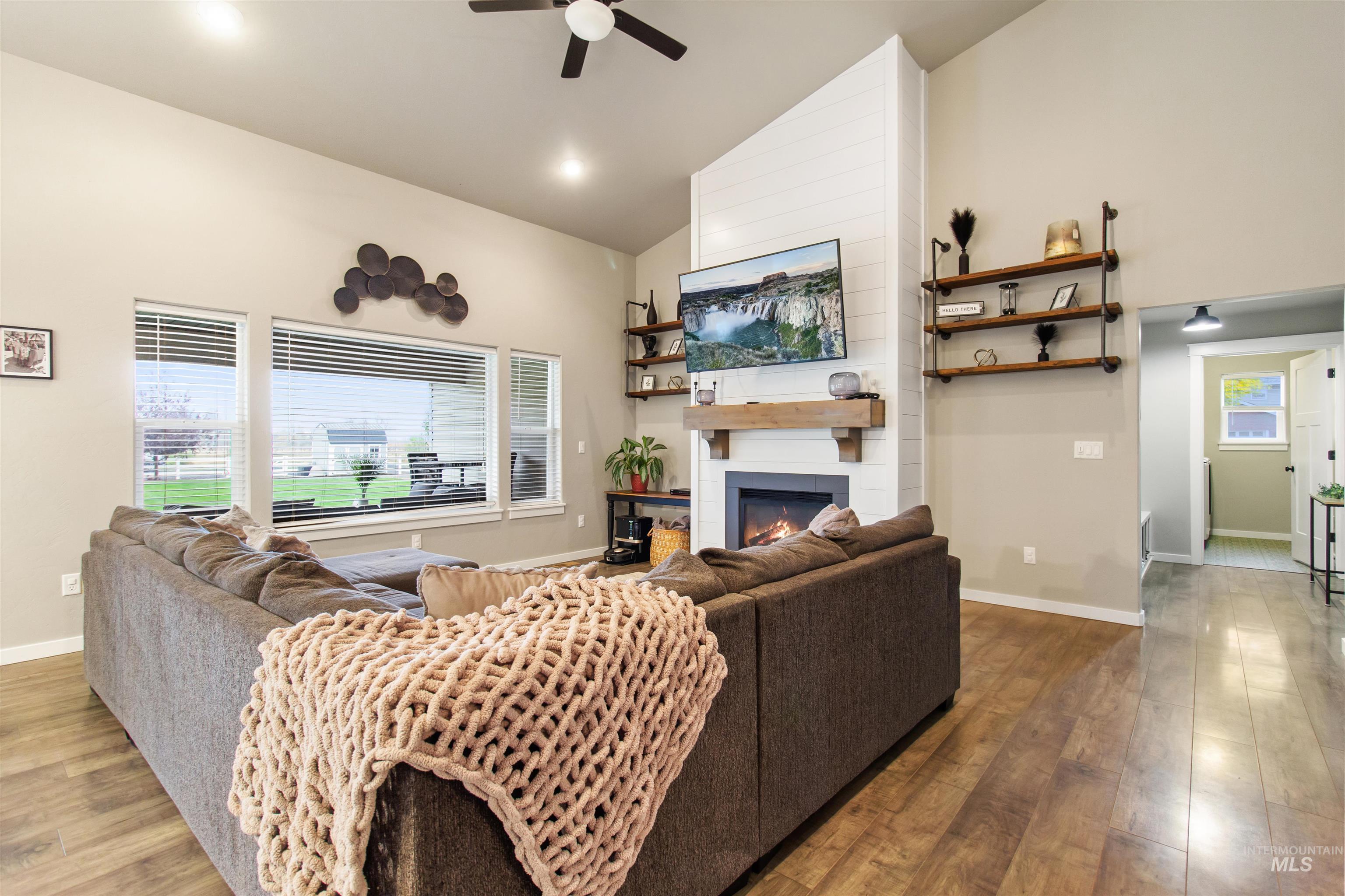Living room with high vaulted ceiling, a large fireplace, light wood-style floors, and ceiling fan