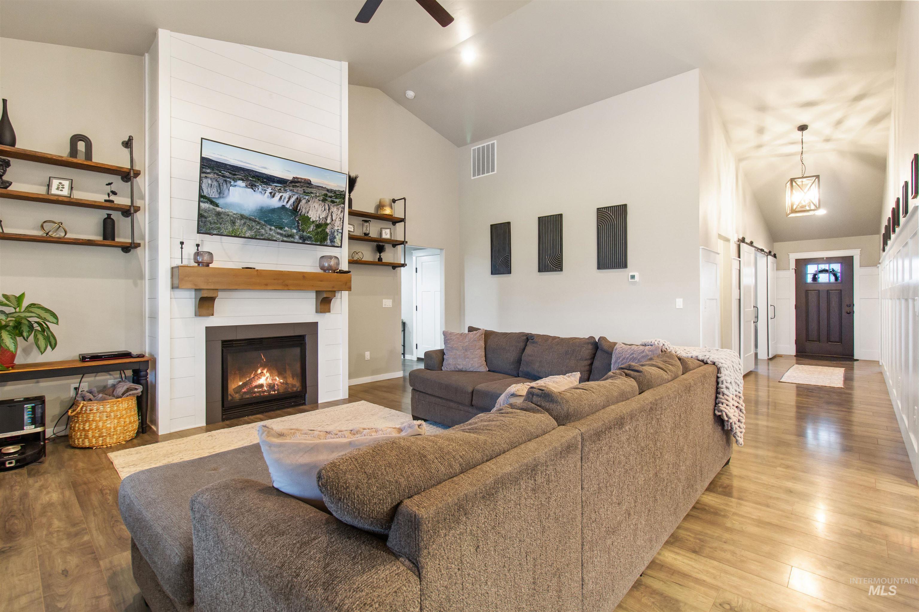 Living room featuring a barn door, wood finished floors, a fireplace, high vaulted ceiling, and ceiling fan