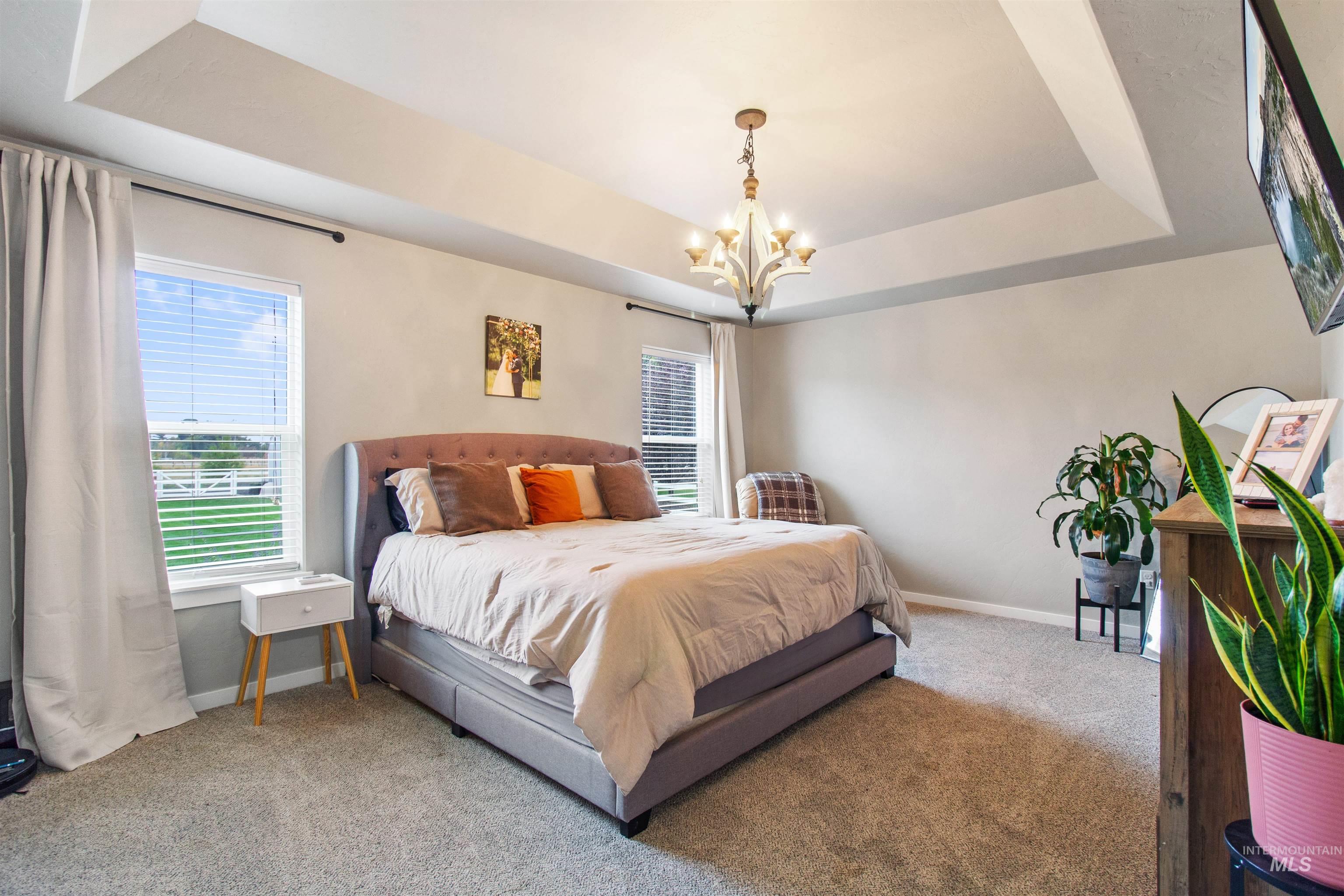 Carpeted bedroom featuring a raised ceiling and a chandelier